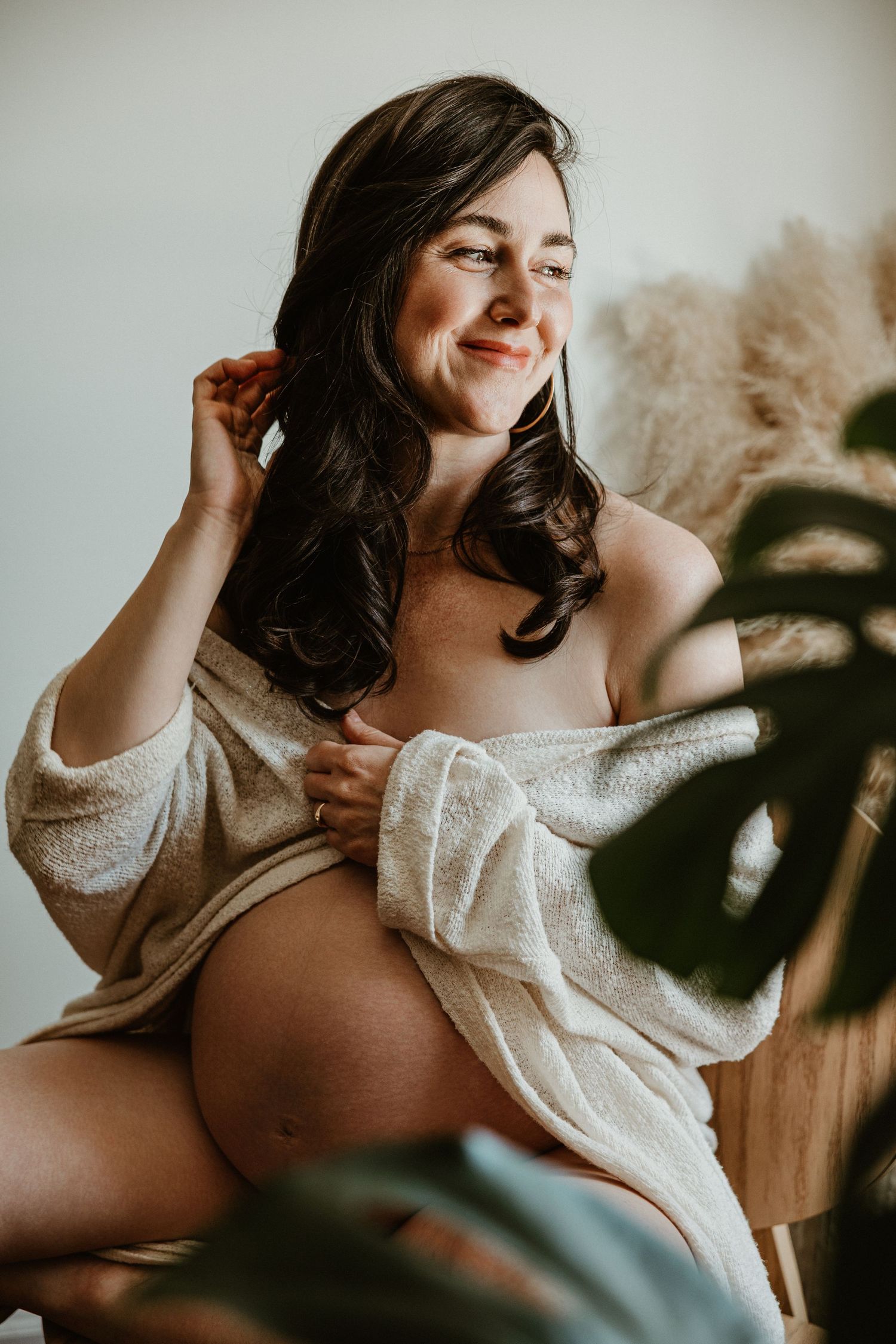 Intimate maternity boudoir photo with soft lighting and pampas grass decor.