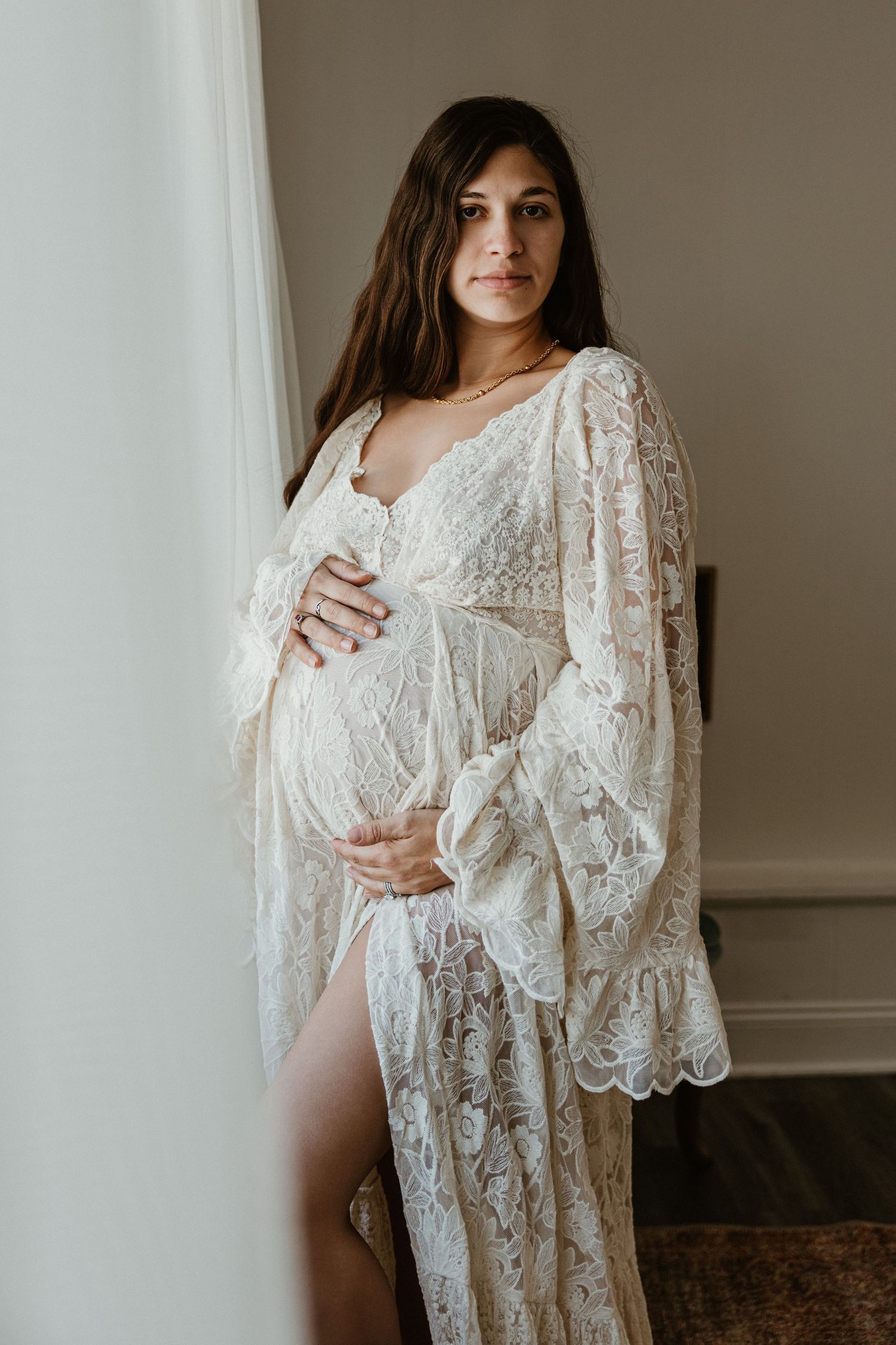 Intimate maternity portrait showcasing a romantic white lace robe in natural light.