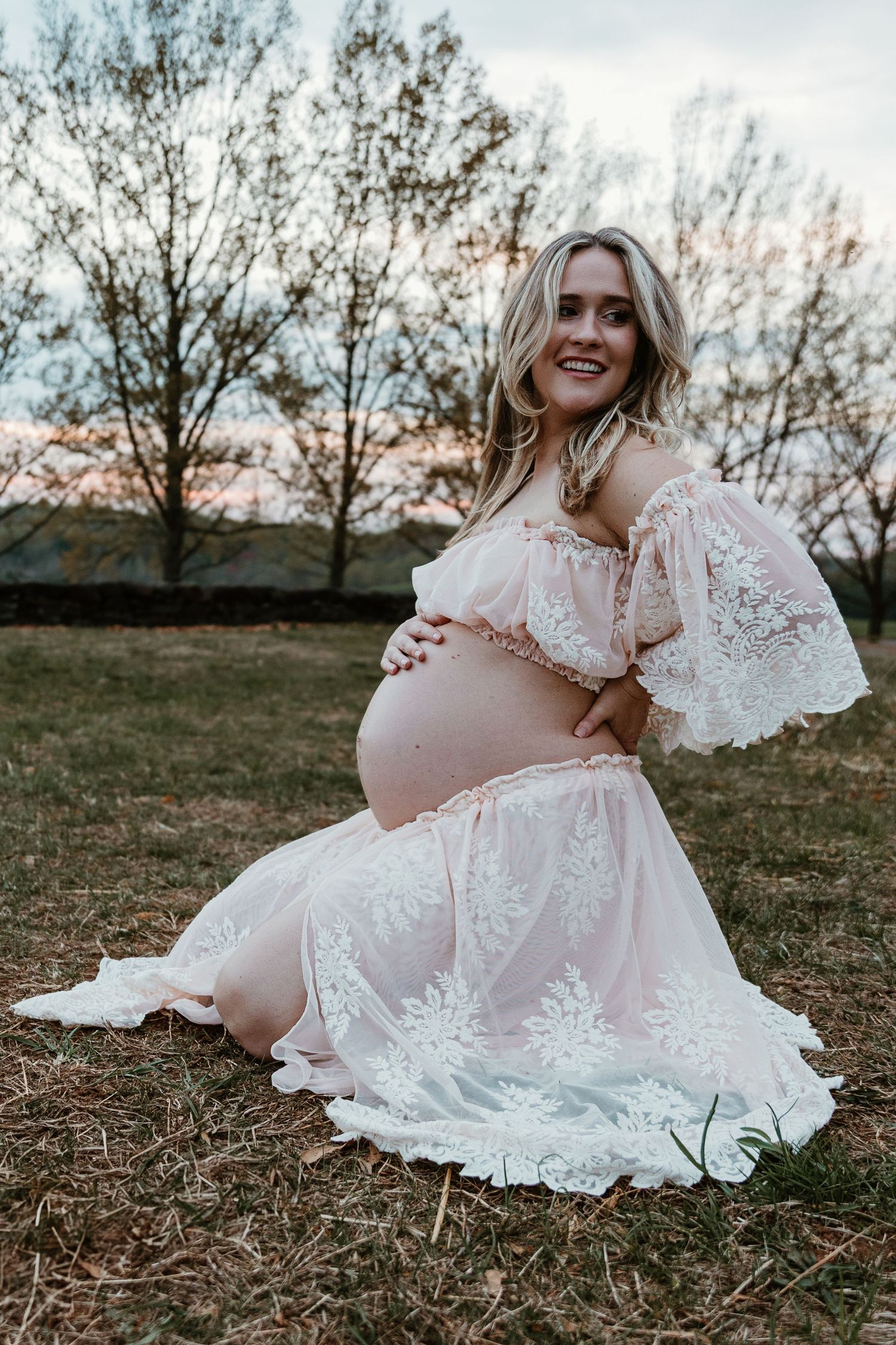 A dreamy maternity portrait featuring a white lace dress in natural outdoor lighting.