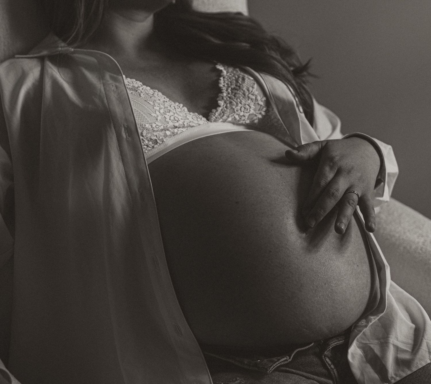Black and white maternity photo of pregnant woman in lace bra and sheer robe cradling her baby bump.