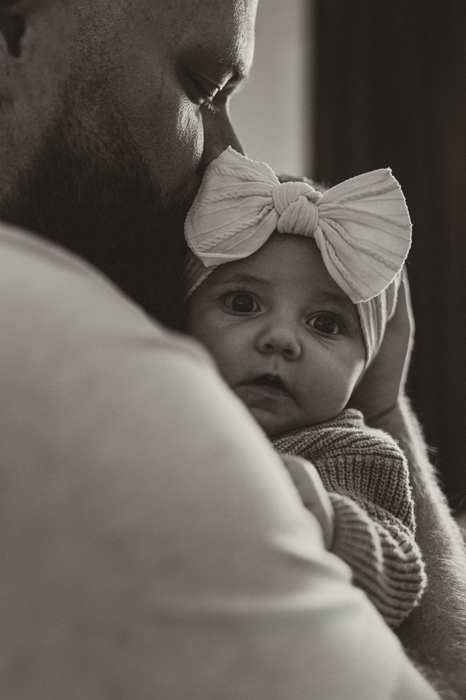 Close-up black and white portrait of a baby wearing a white bow headband.