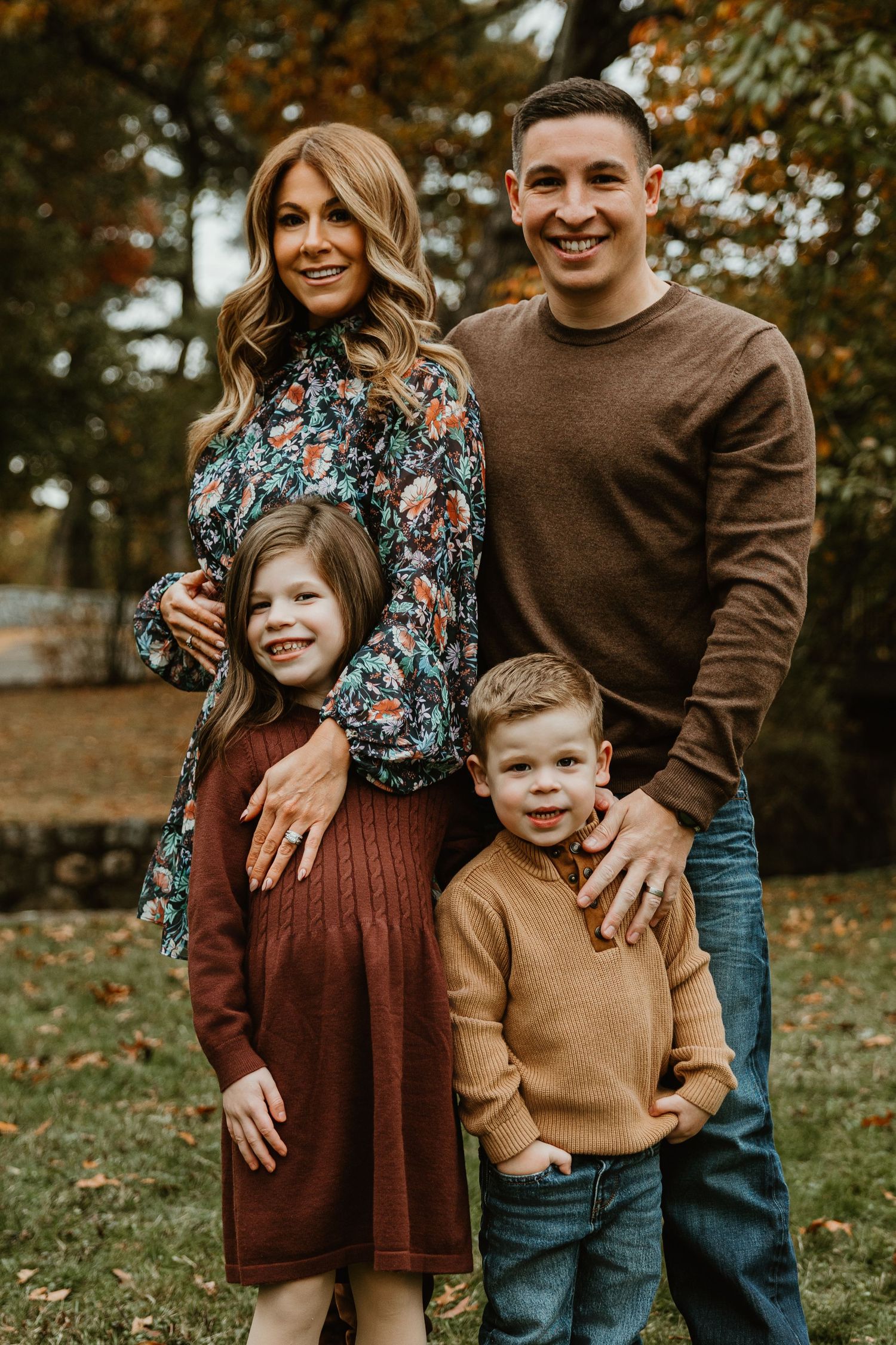Family poses together outdoors in coordinated fall outfits with autumn foliage in background.