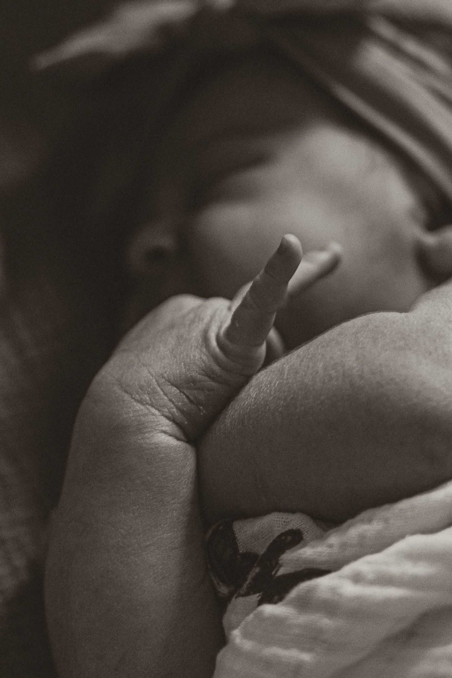 Black and white close-up photo of a sleeping newborn baby with tiny fingers and delicate features.