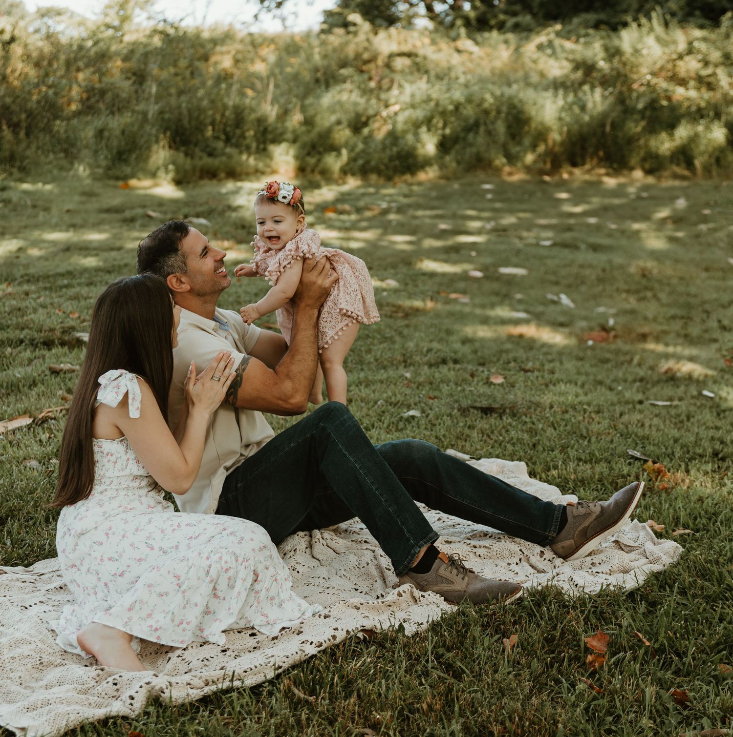 Family having playful moments on picnic blanket in park.