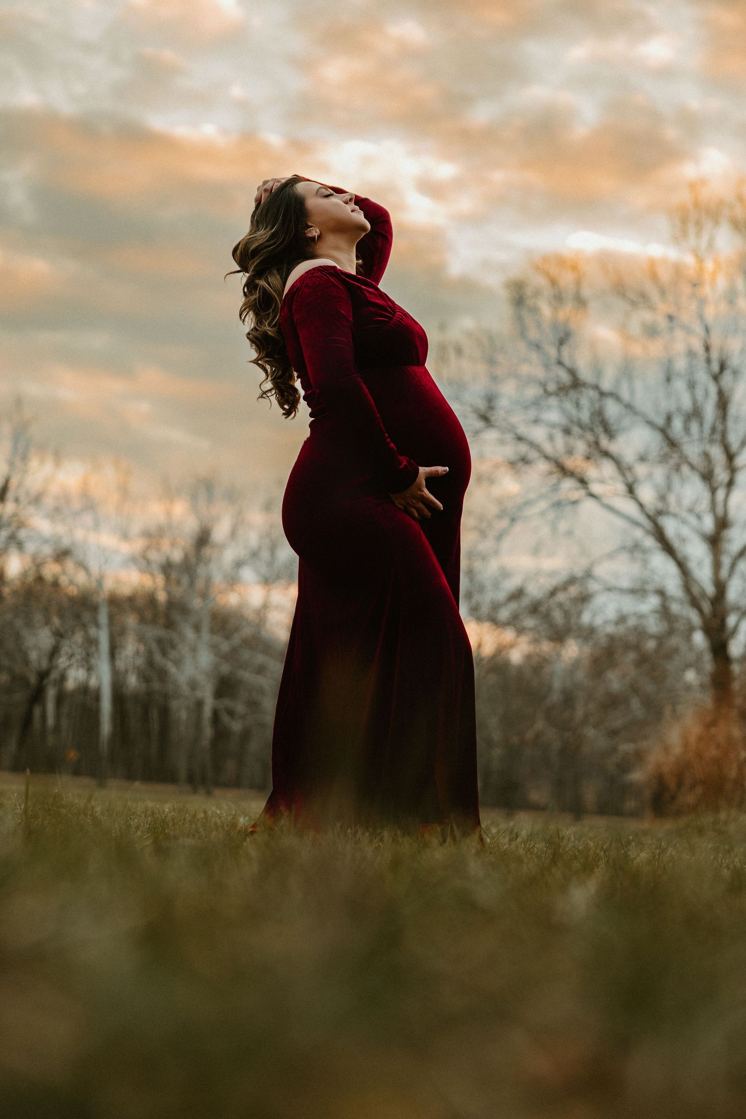 Figure in a flowing red dress stands gracefully in a misty autumn field during golden hour.