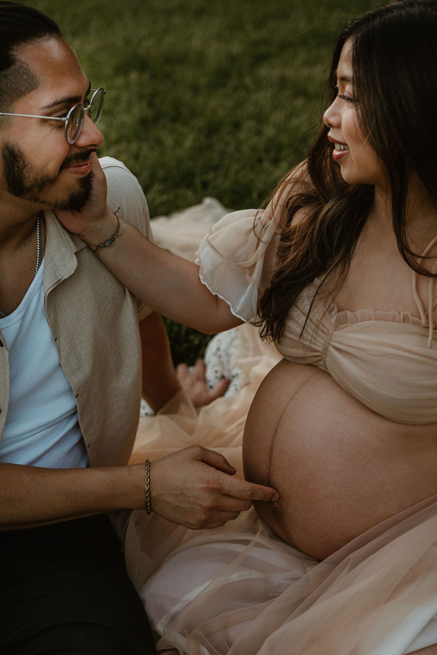 A couple shares a joyful moment outdoors, with the man tenderly touching the pregnant woman's bare belly.