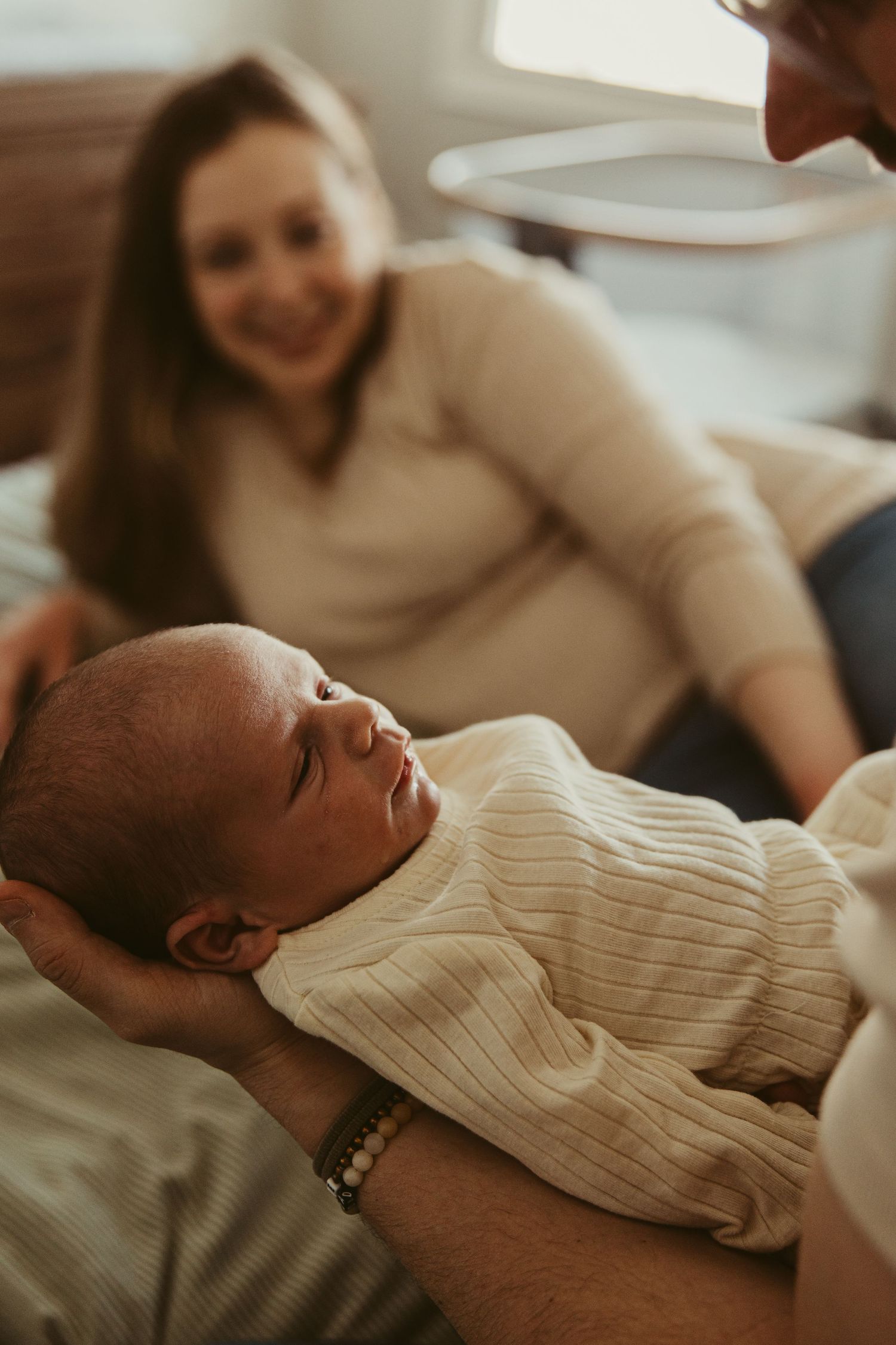 Infant in white sweater being held while parents look on lovingly.