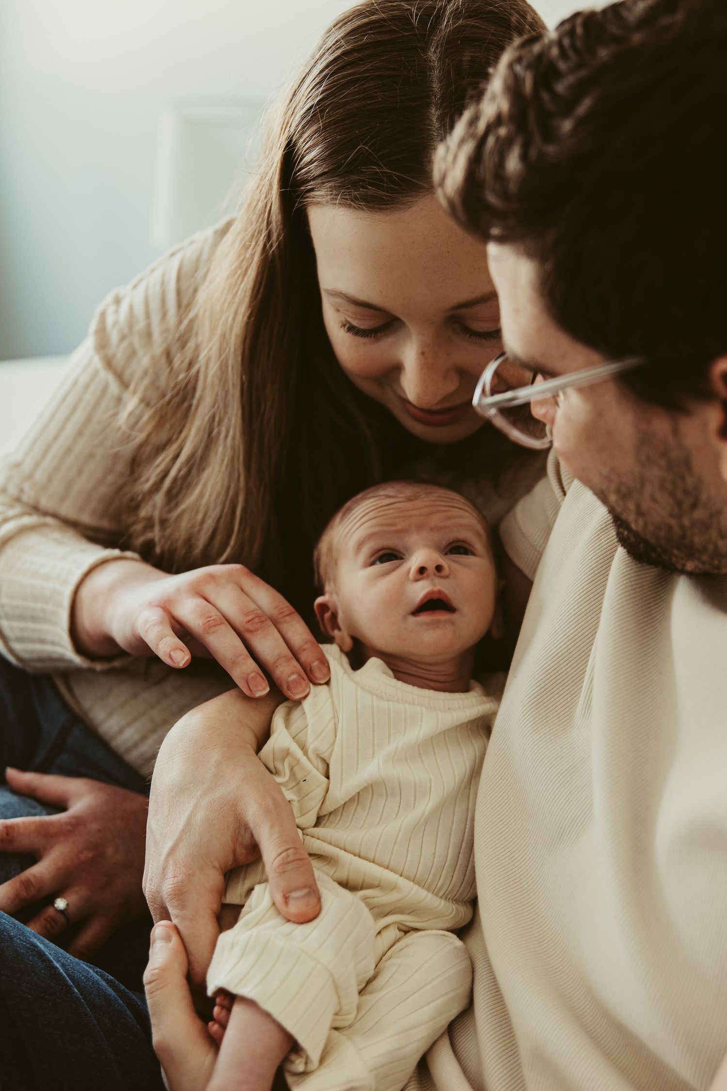 Progressive shots of parents holding and bonding with their newborn baby wearing cream-colored clothing.