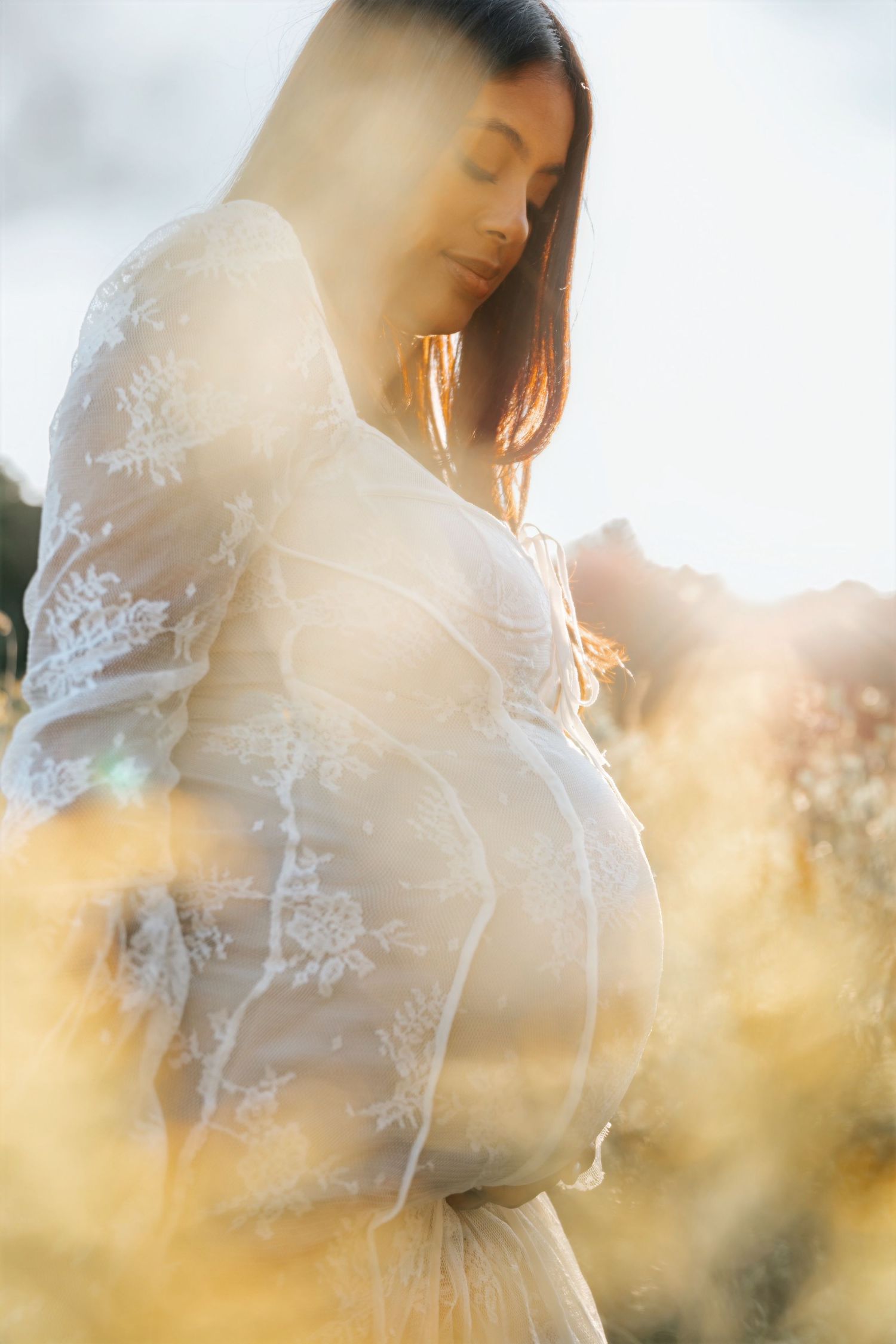Ethereal sunlit portrait of a delicate white lace dress against a dreamy outdoor background.