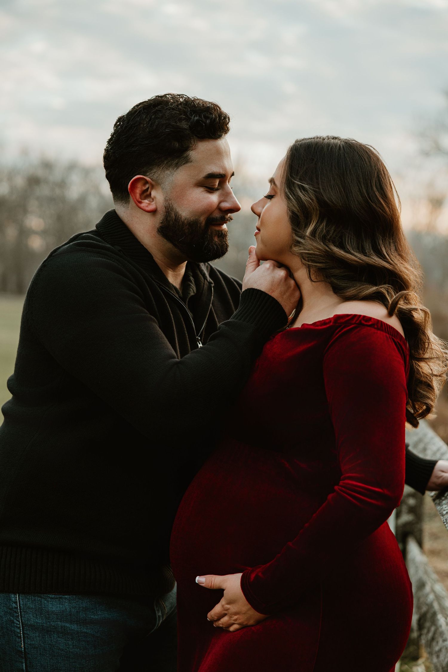 Romantic couple embraces in a moody outdoor photoshoot wearing burgundy and black.