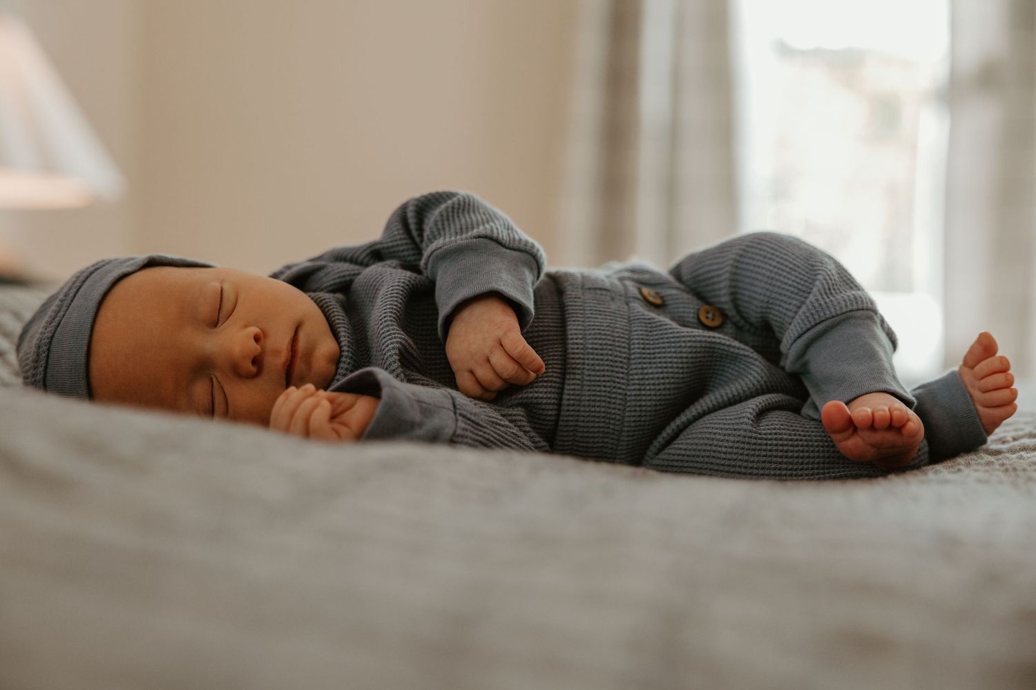 Peaceful newborn sleeping on soft grey bedding in natural light.