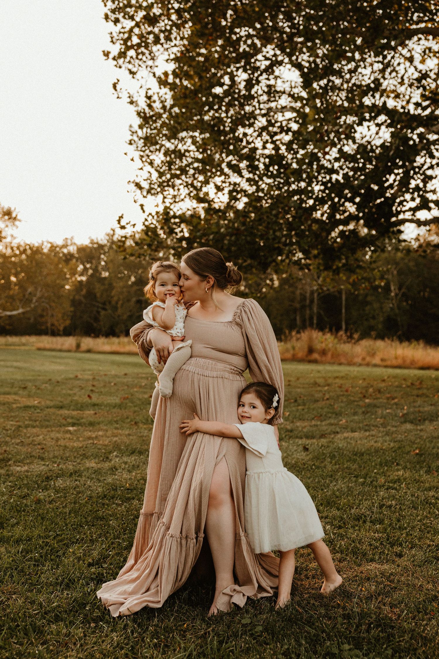 Tender family moment captured in soft beige tones during sunset in an open field.
