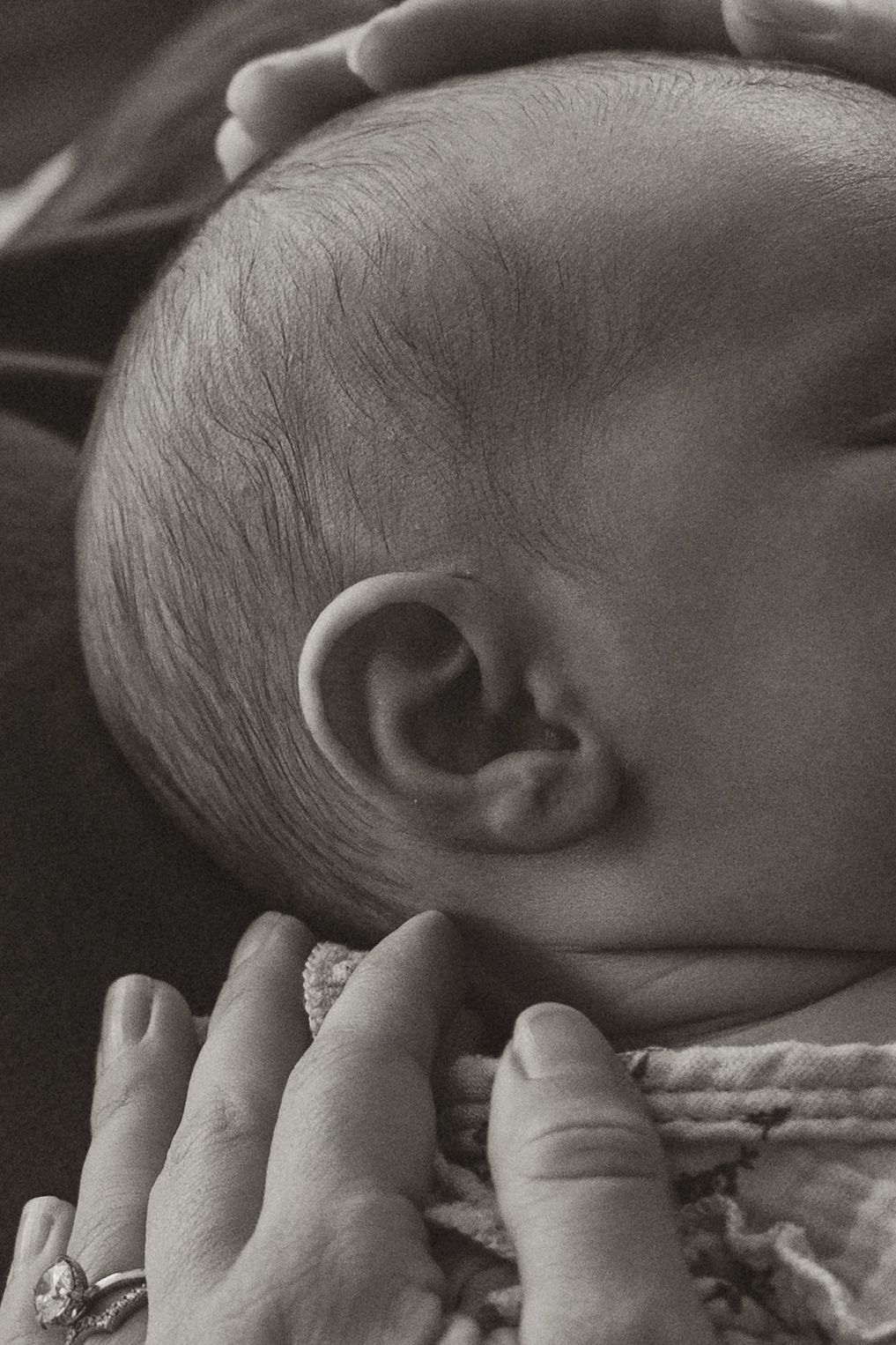 Close-up black and white photo of a sleeping newborn baby cradled in an adult's hands wearing a diamond ring.