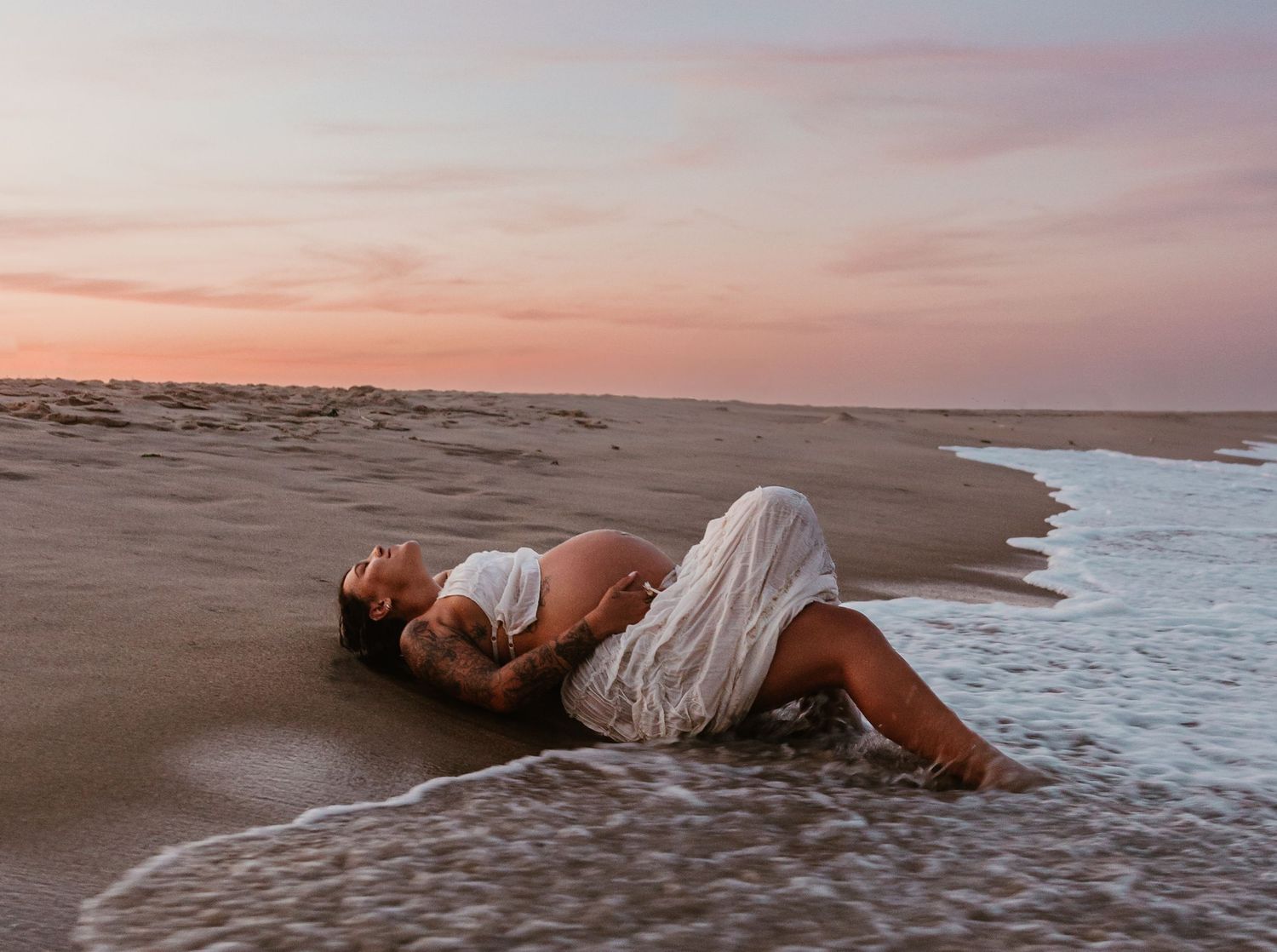 Dramatic beach maternity photos with waves during golden hour.
