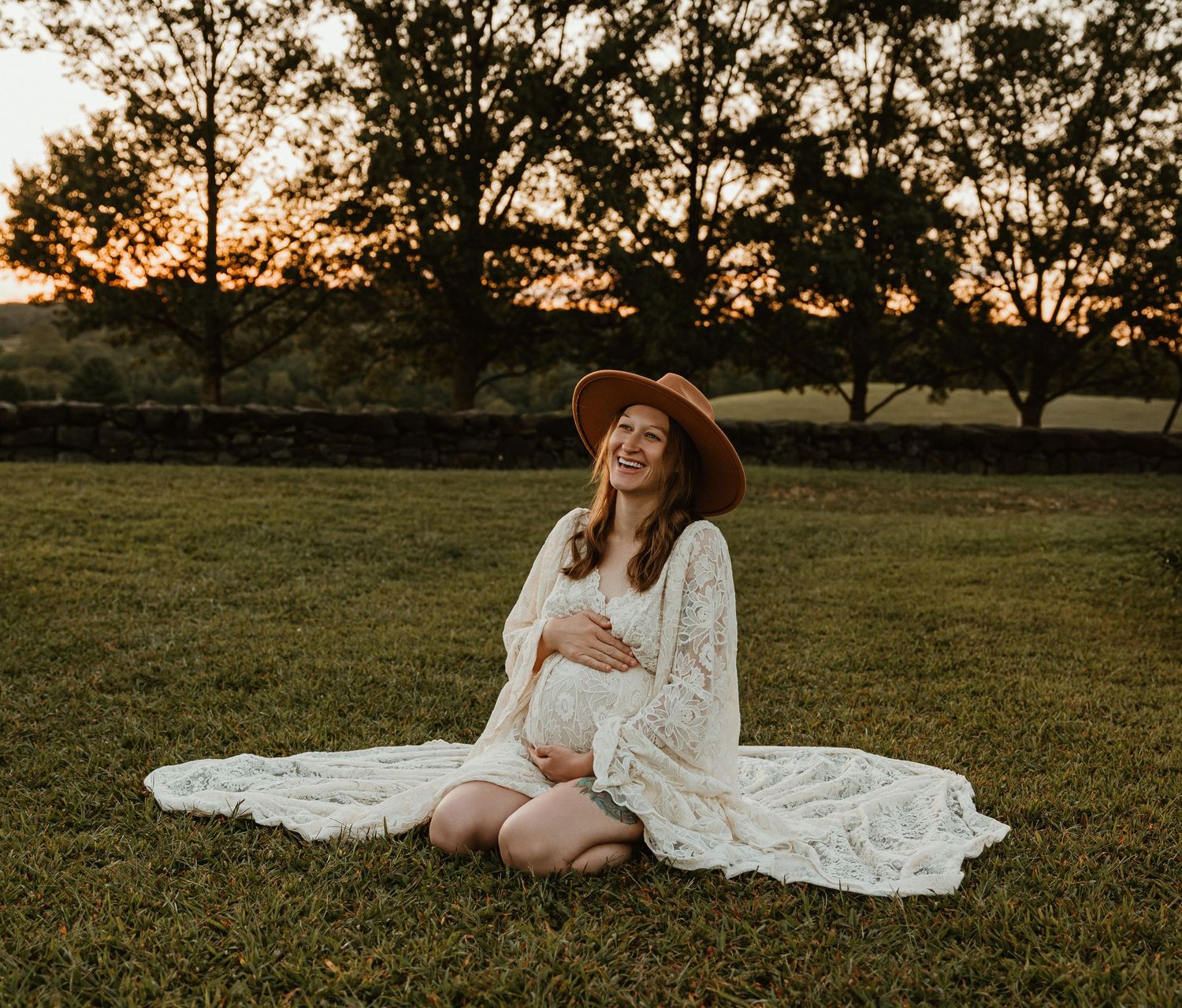 Maternity photography session in a grassy field during sunset with a flowing white lace dress.