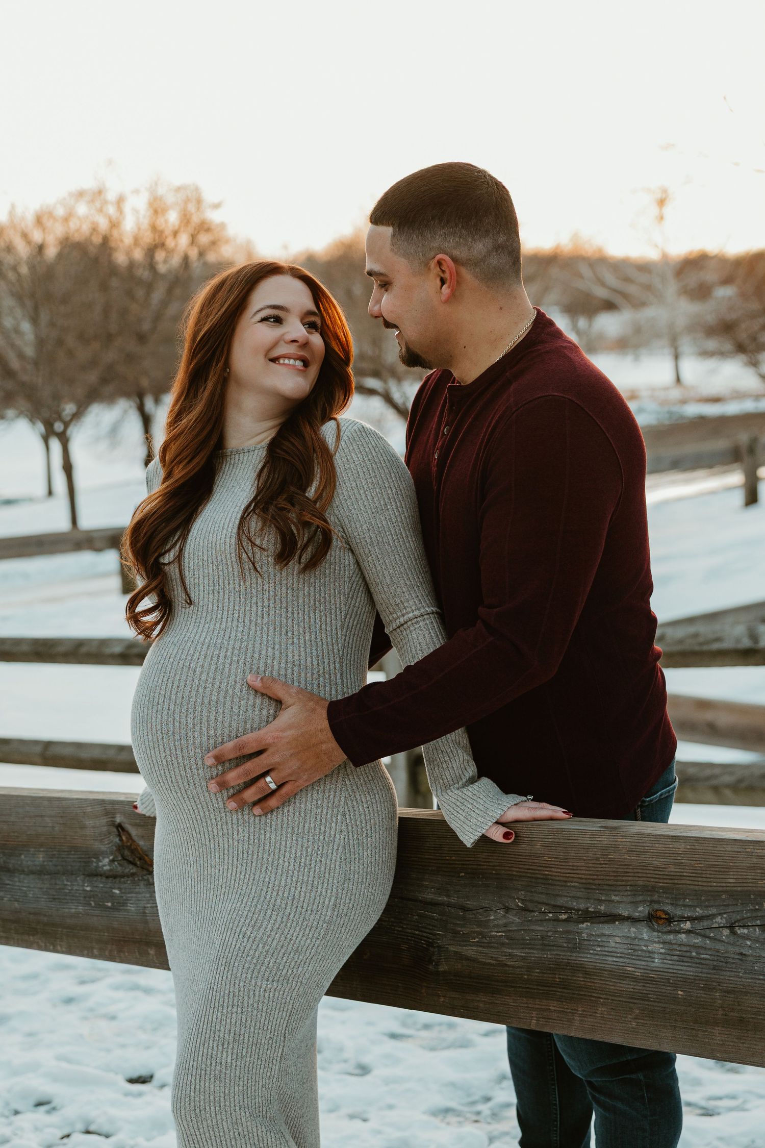 Maternity photo session in winter with couple by wooden fence.