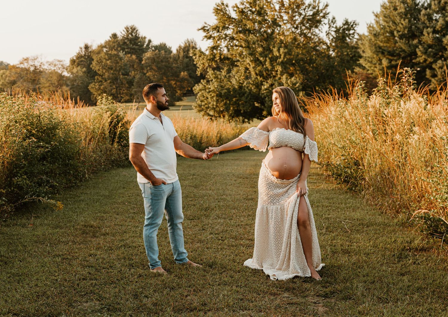 Couple holding hands in field during sunset maternity photoshoot.