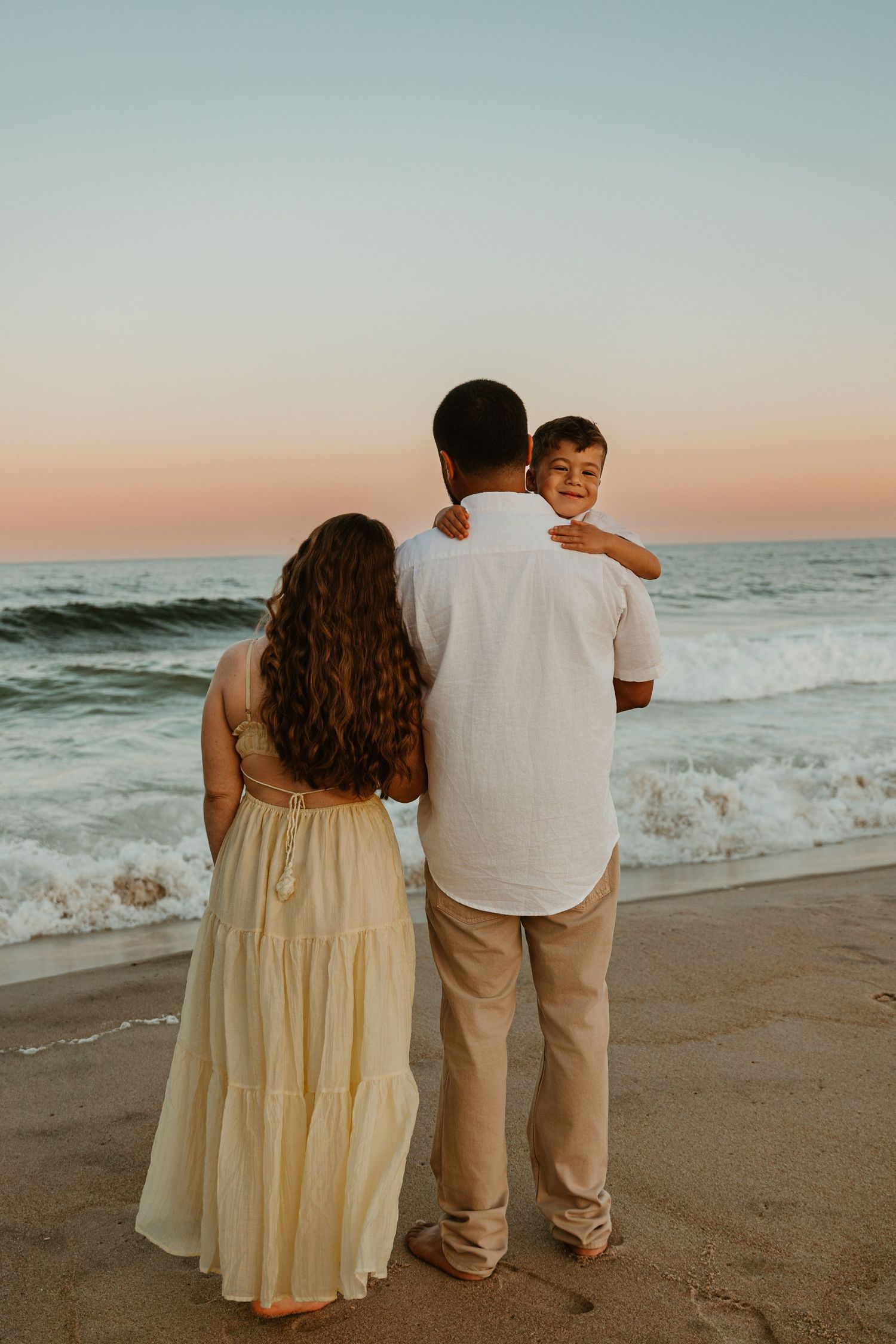 A family stands together on the beach watching the sunset over the ocean waves.