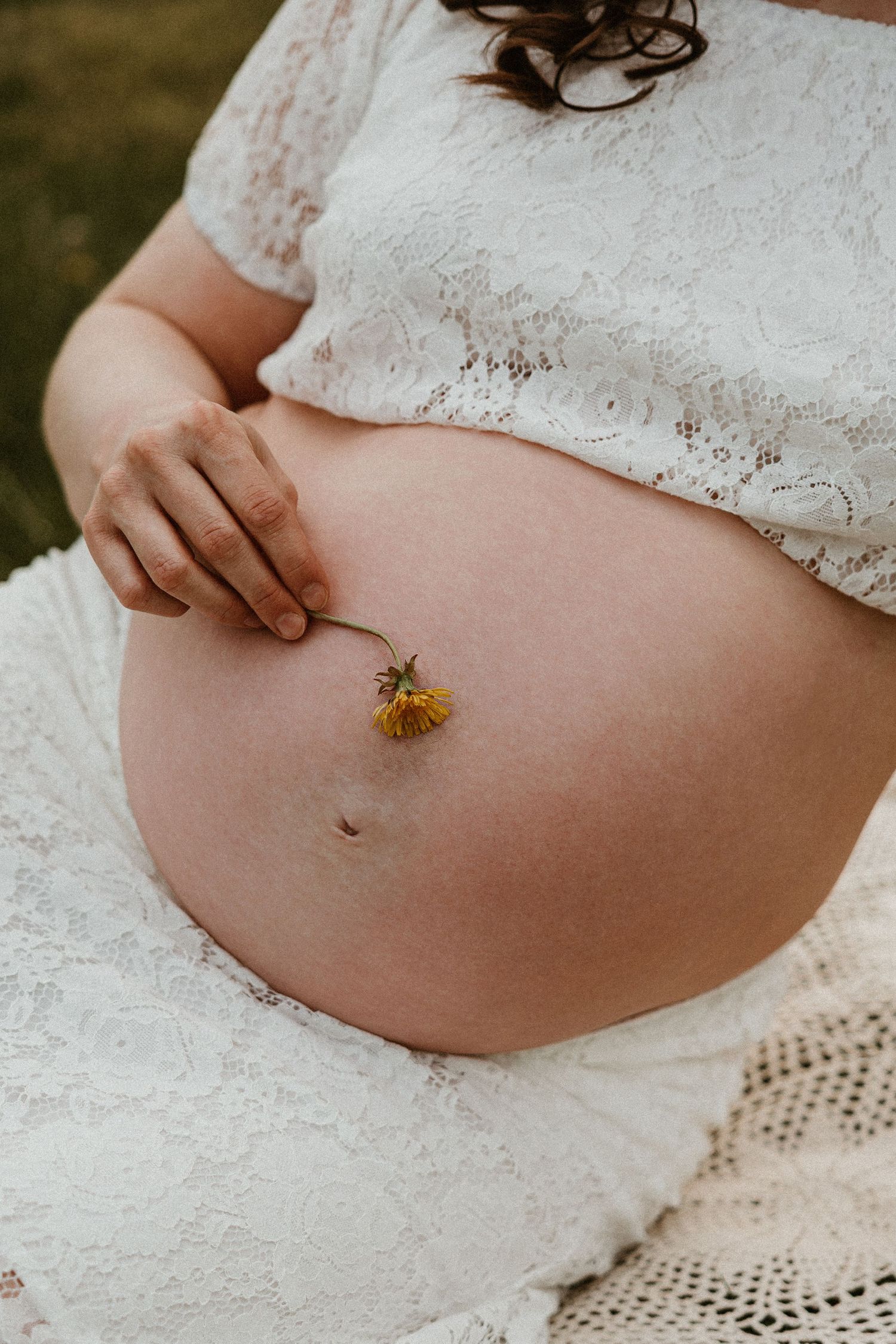 Close-up of pregnant belly with a delicate yellow flower during maternity session.