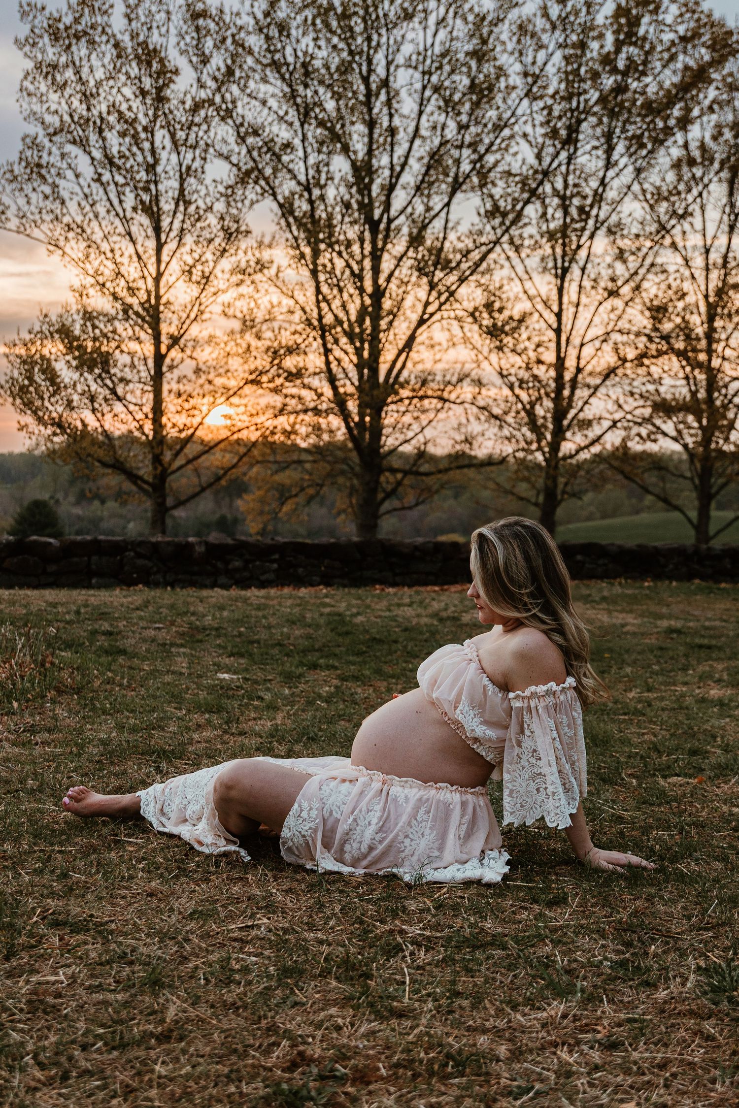 A white lace dress glows in the warm light of sunset against silhouetted trees.