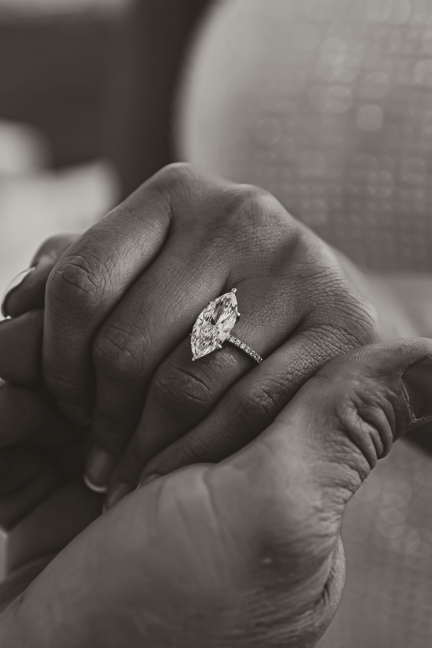 Black and white photo of a marquise diamond ring on hand against soft fabric.