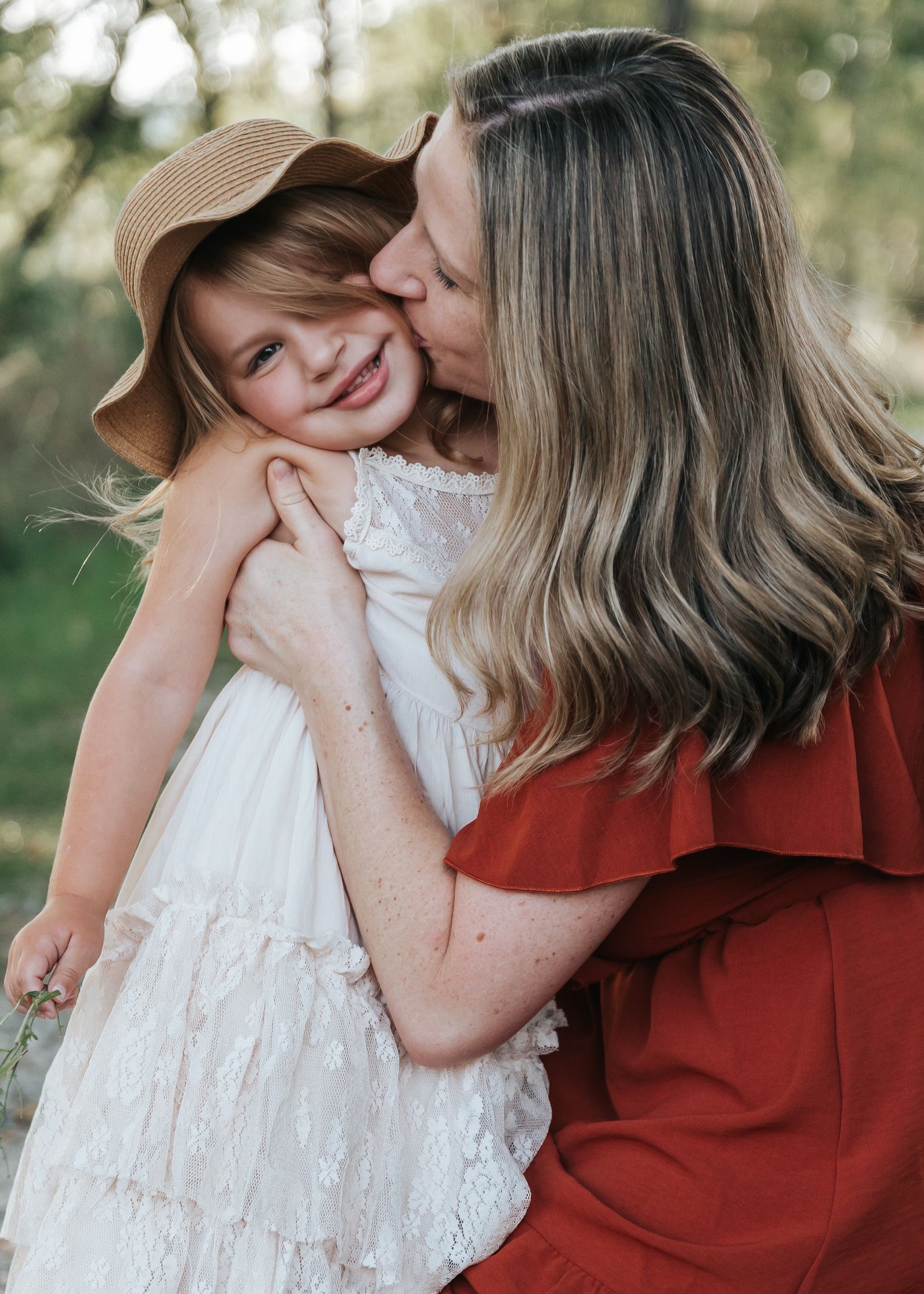 A tender moment captured between parent and child in white lace dress against a natural outdoor setting.
