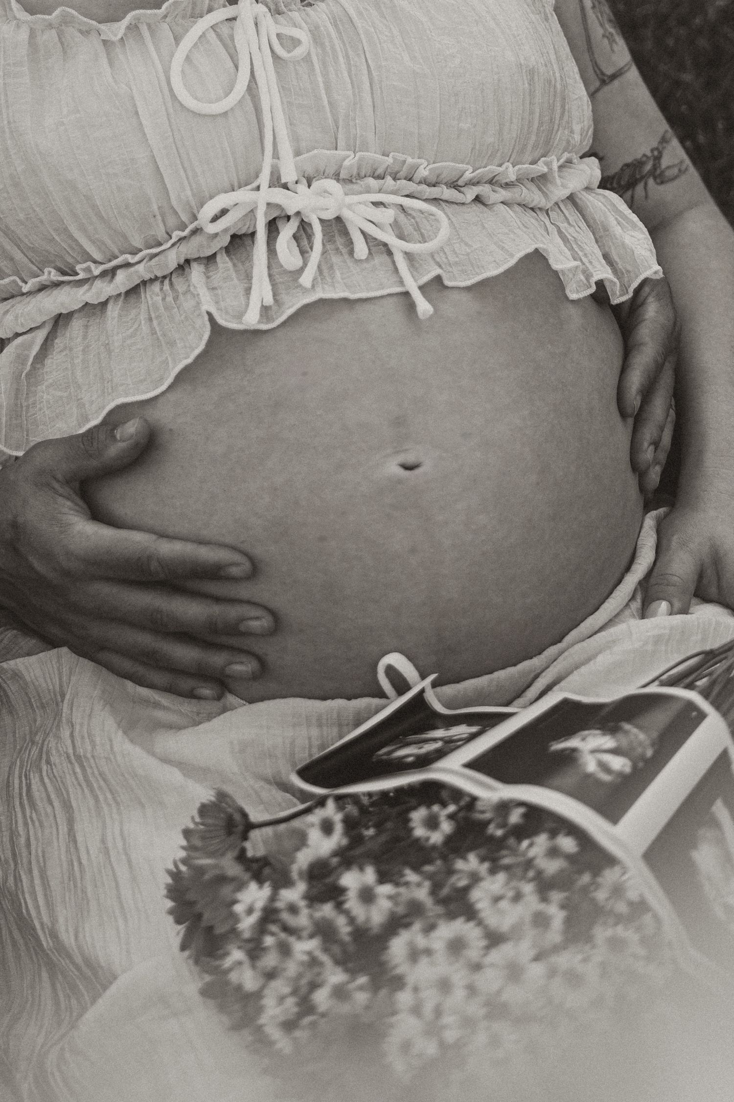 Black and white maternity photo showing pregnant belly with ultrasound photo and wildflower bouquet.