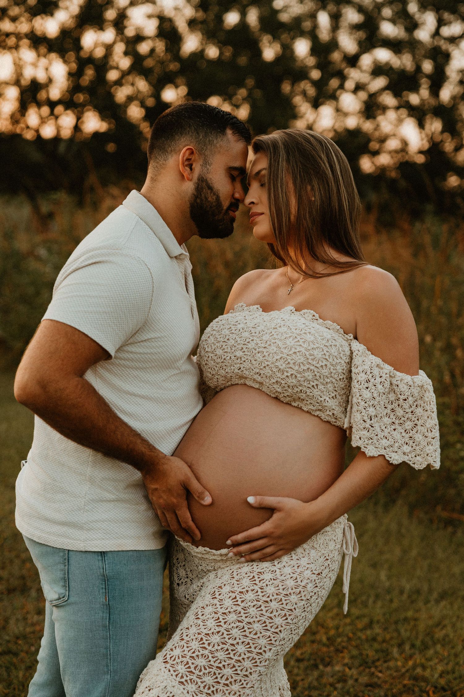 Intimate maternity photo of couple in white outfits embracing at sunset.