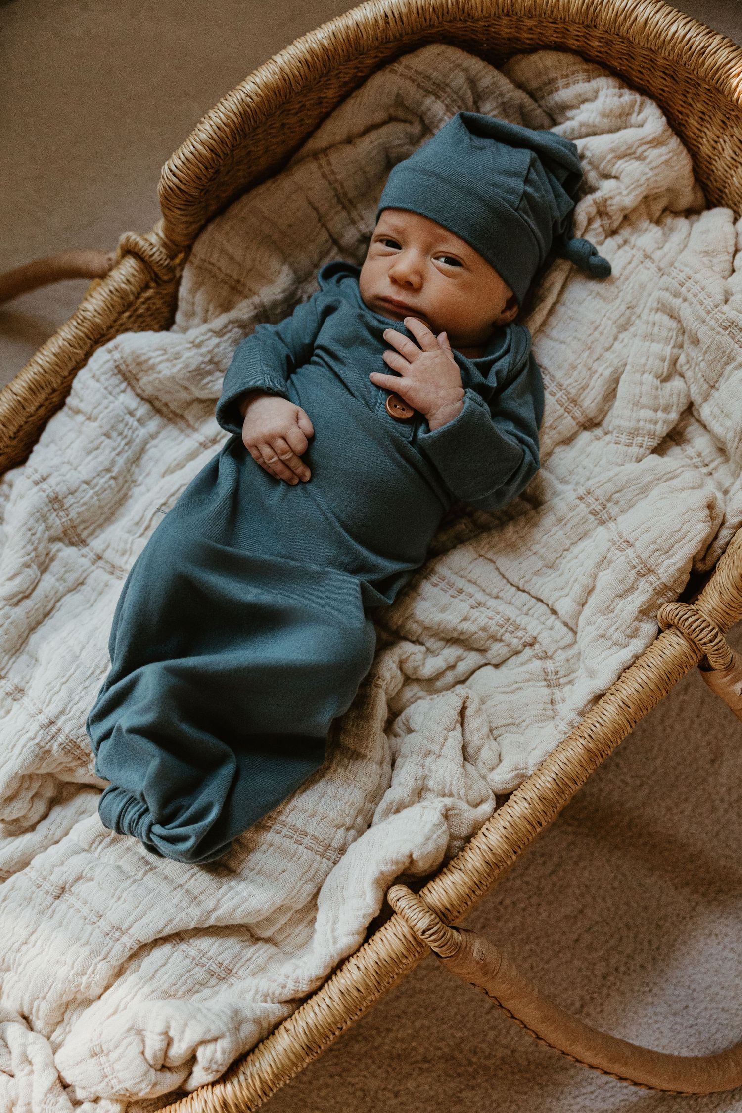 Newborn baby sleeping peacefully in a woven basket on a textured blanket.