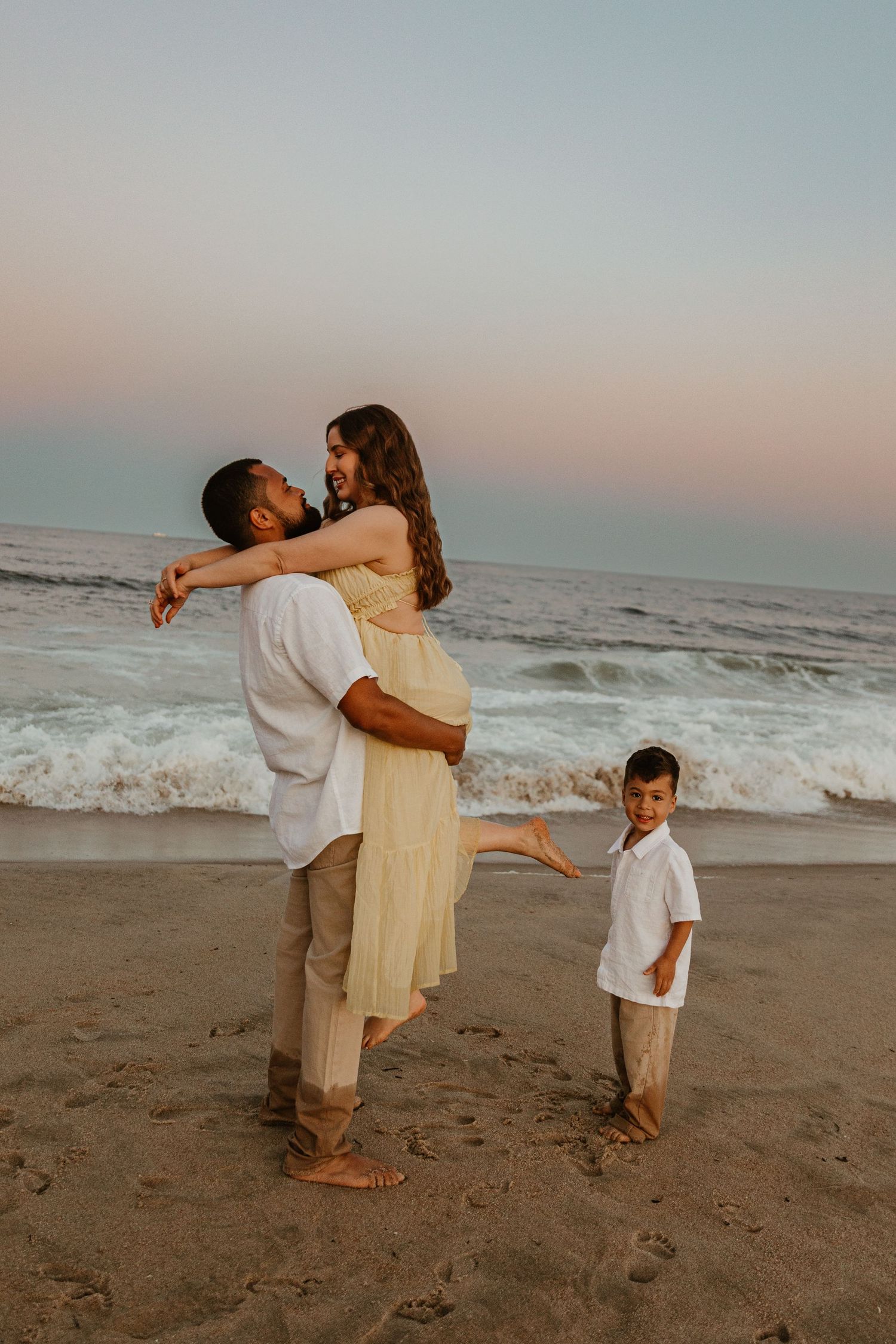 A loving family moment captured on the beach at sunset with crashing waves behind them.