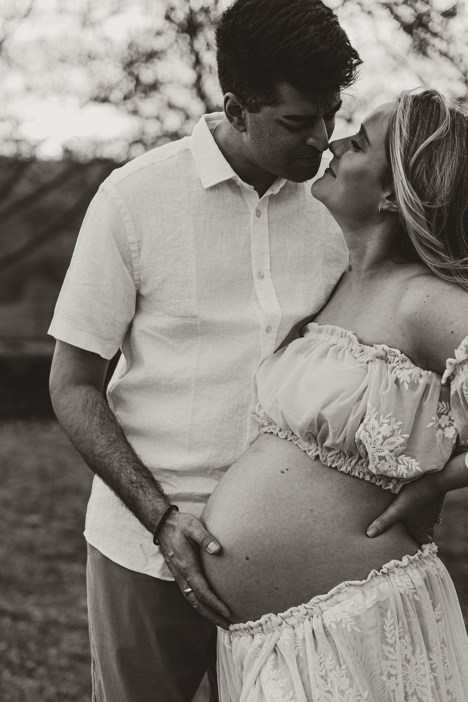An intimate maternity photo showing a couple in white clothing at sunset.