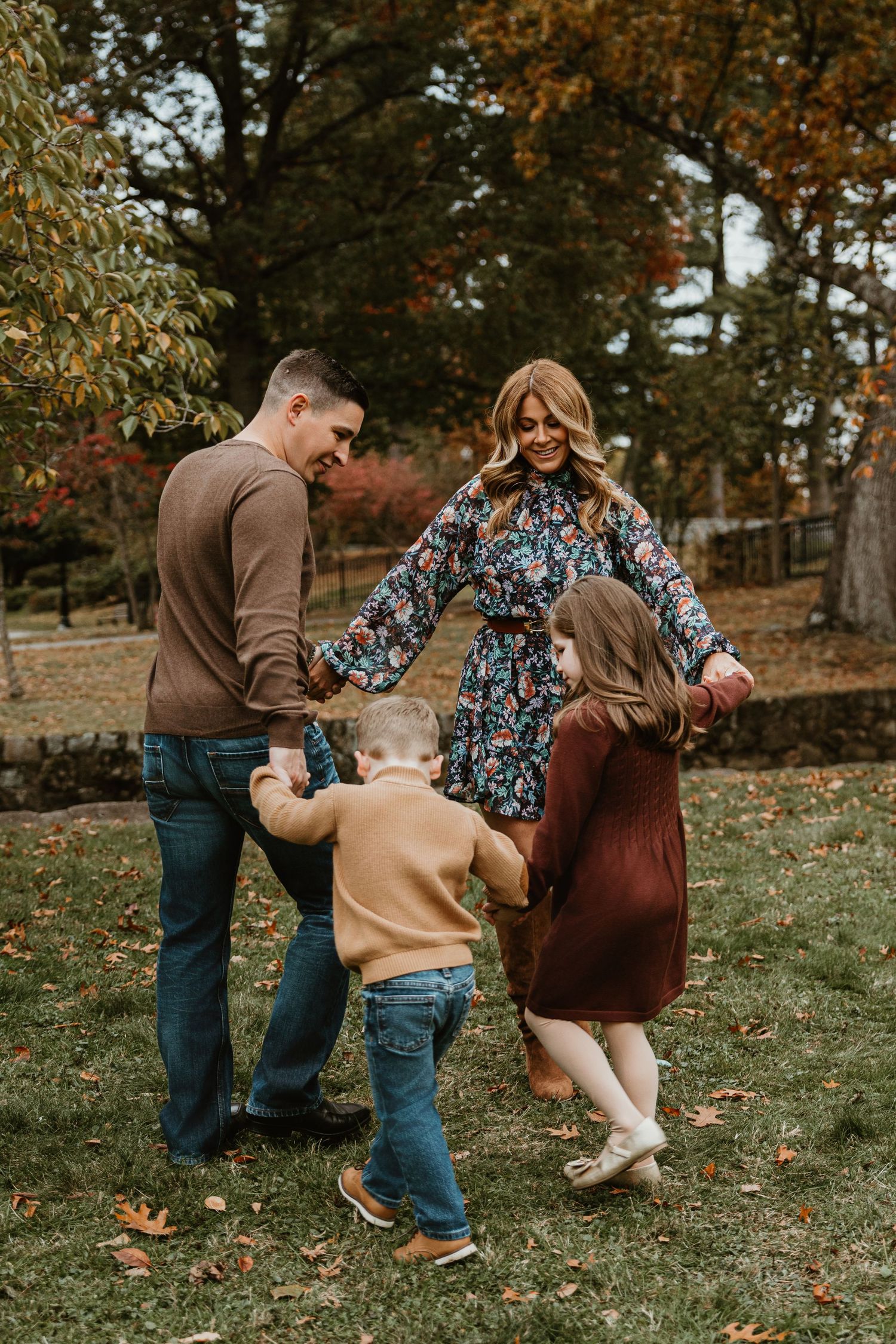 Family plays and laughs together in autumn leaves wearing coordinated brown and floral outfits.