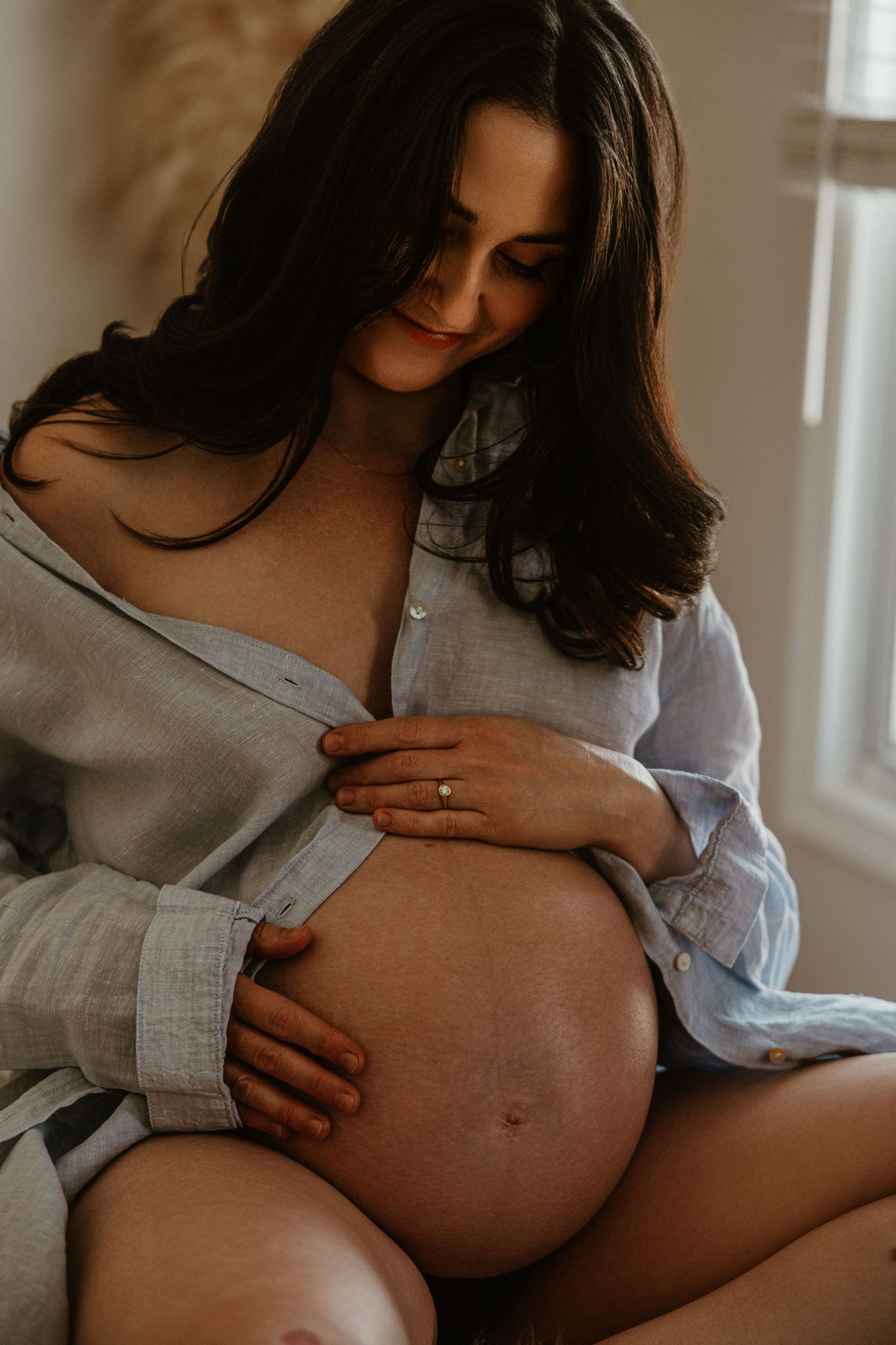 Intimate maternity portrait in soft gray sweater by window light.