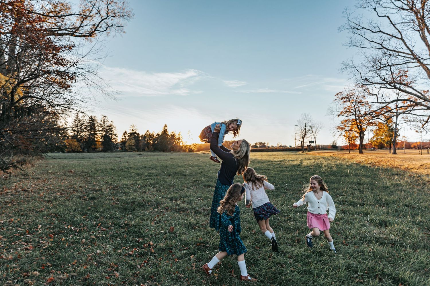 Wide landscape shots of a family playing together in an open field at sunset.