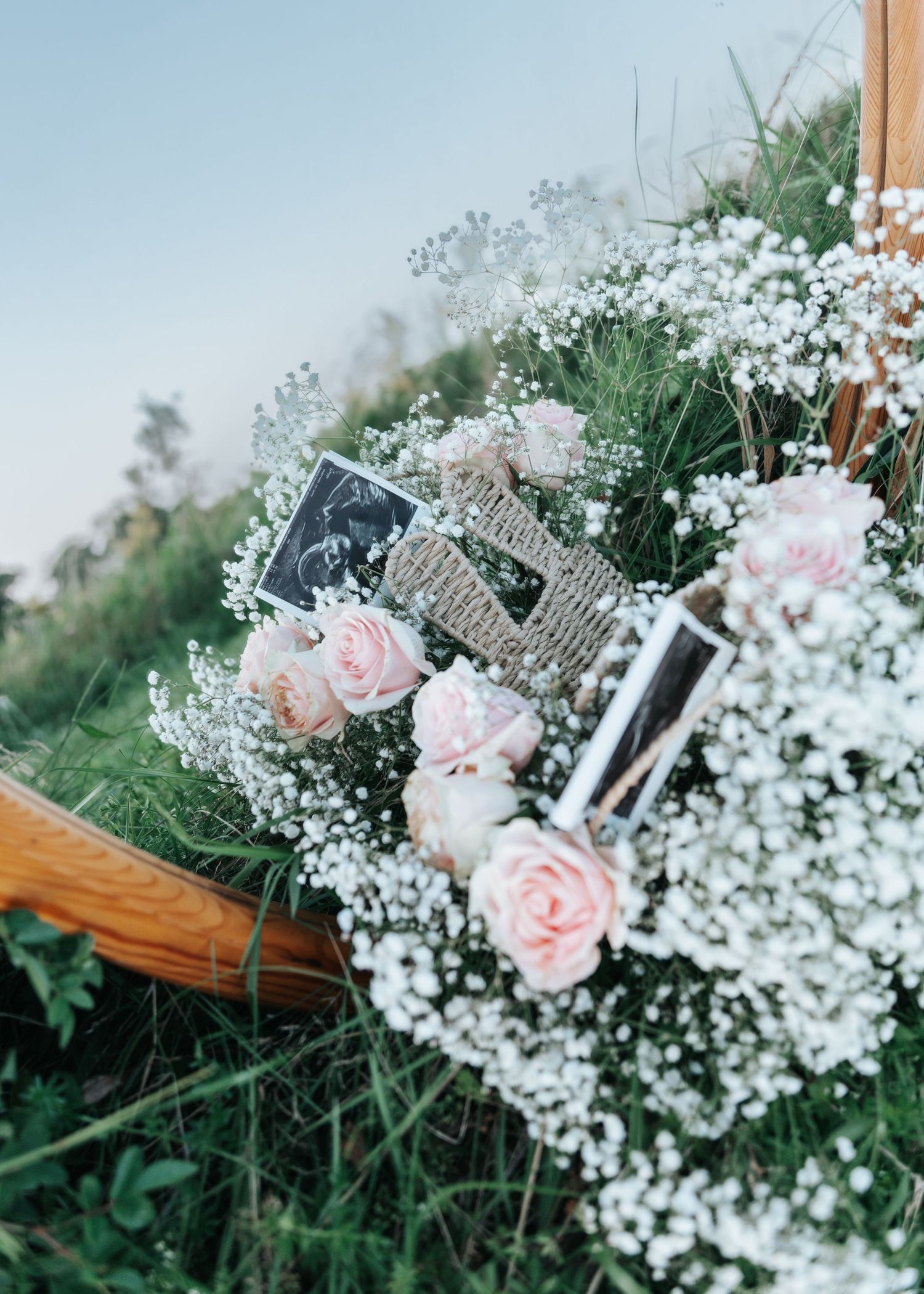 Romantic arrangement of pink roses and ultrasound photos in a wicker basket with baby's breath.