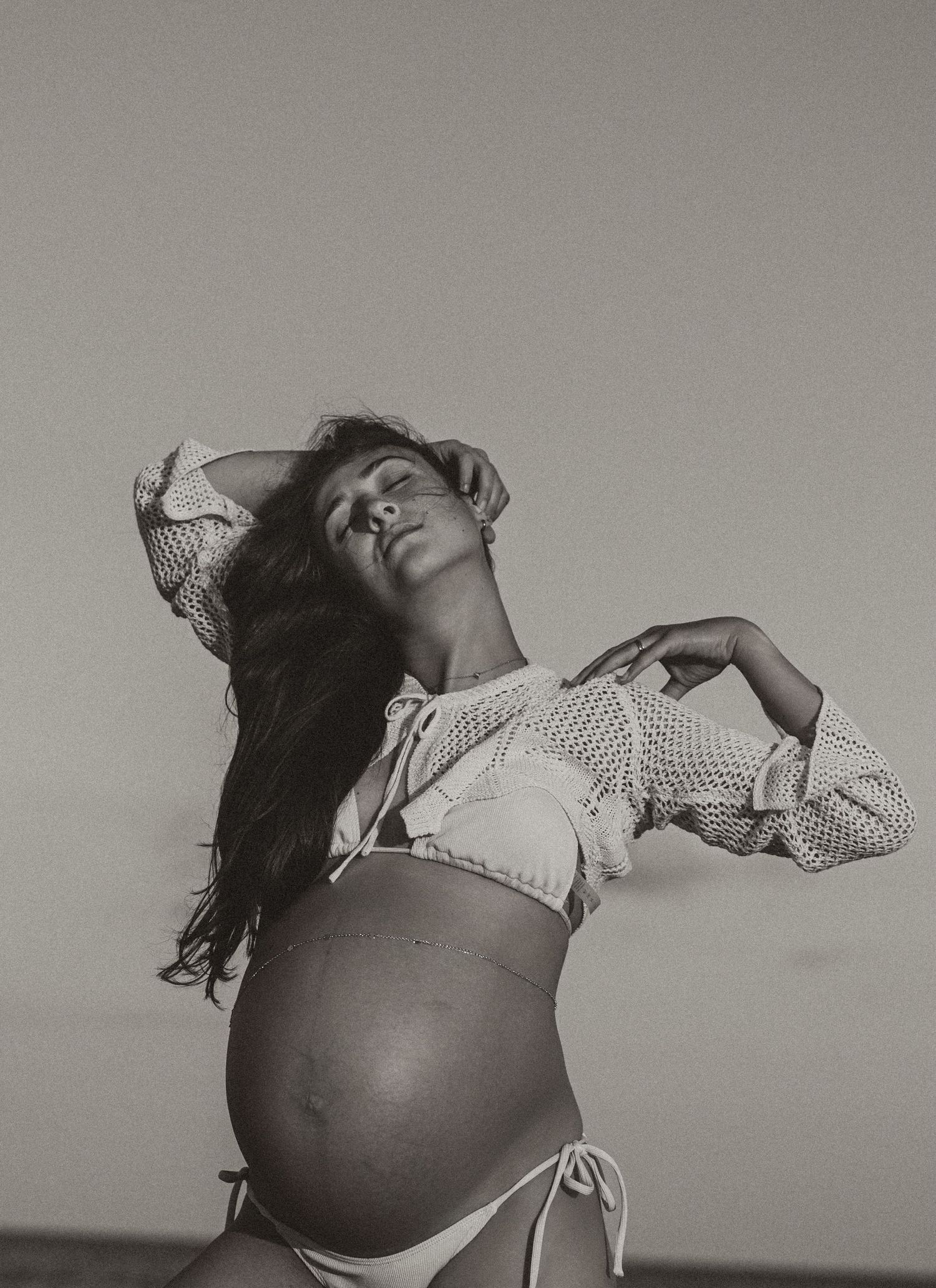 Black and white maternity photo of pregnant woman posing on beach.