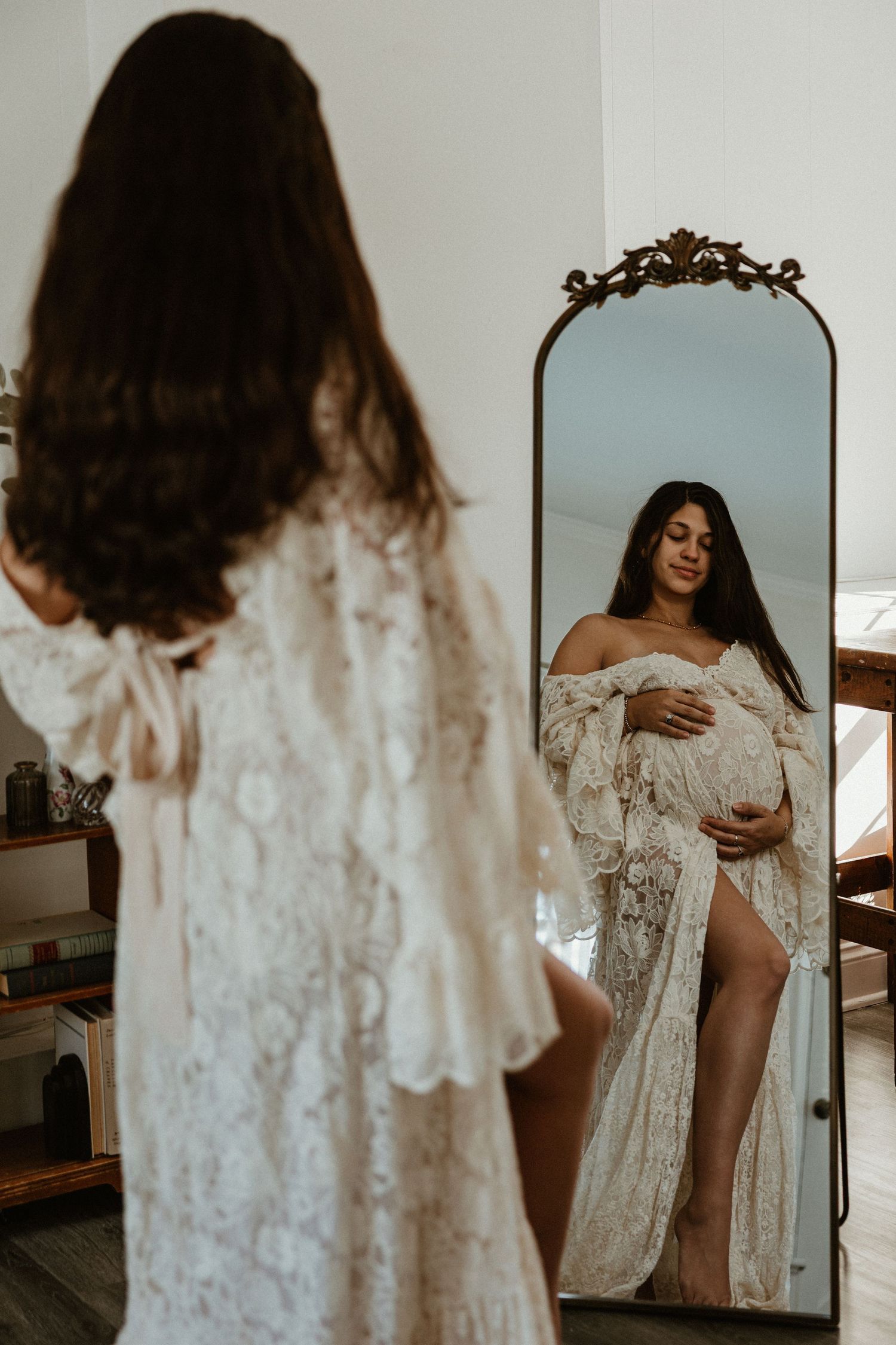 Artistic maternity boudoir session with vintage mirror and flowing lace dress.