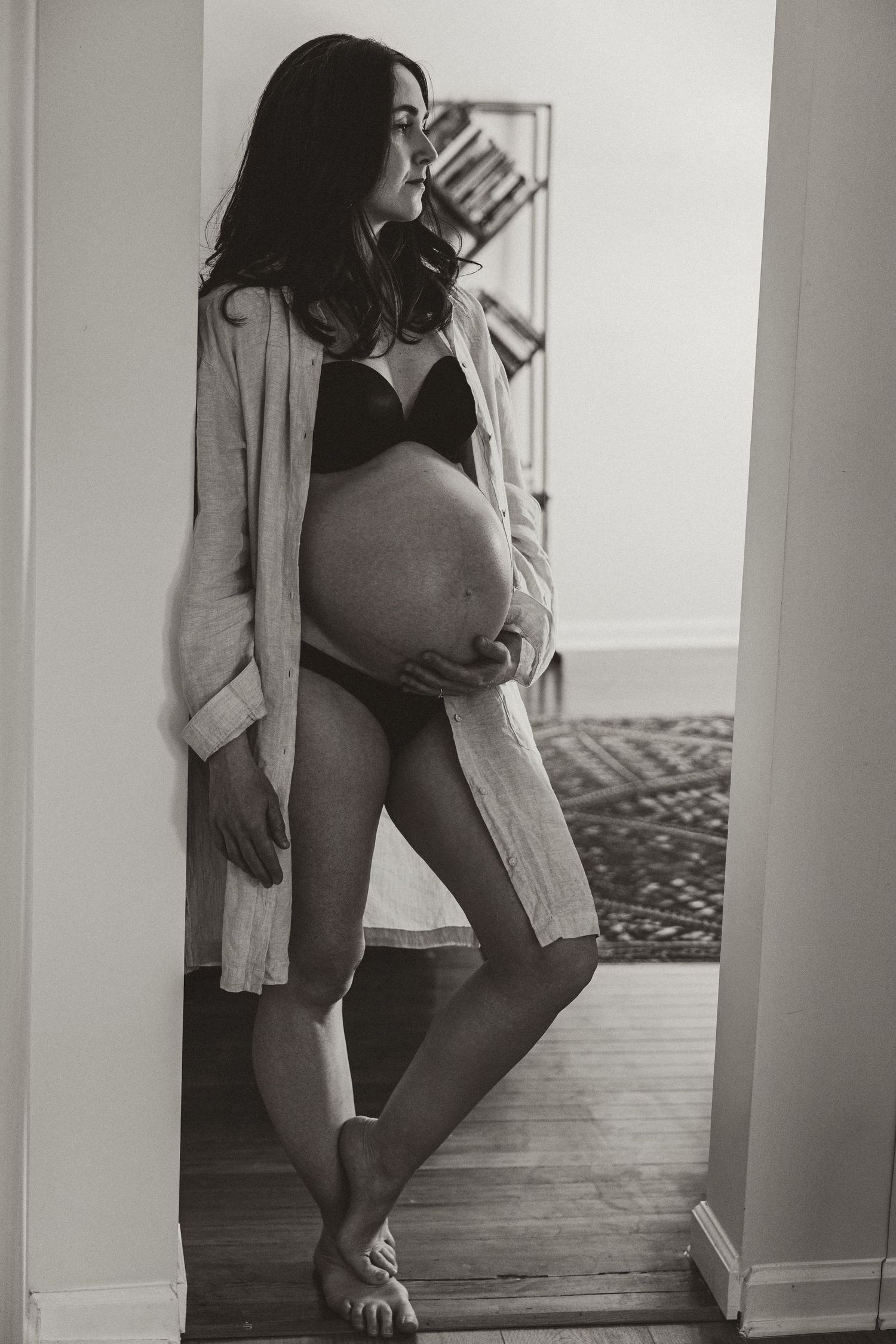Black and white maternity photo showing pregnant silhouette in intimate indoor setting.