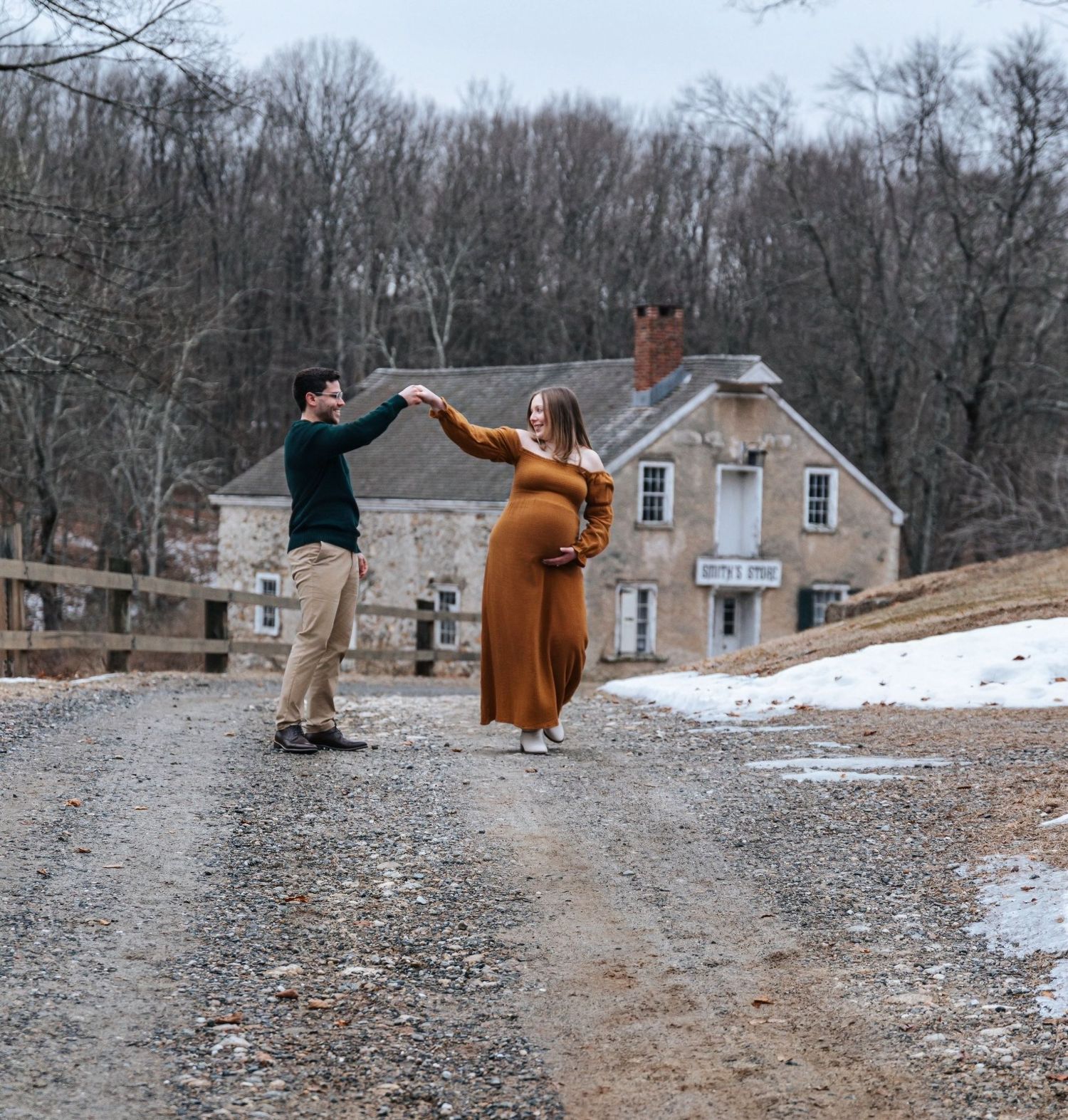 Couple dancing playfully on a gravel path with houses in the winter background.