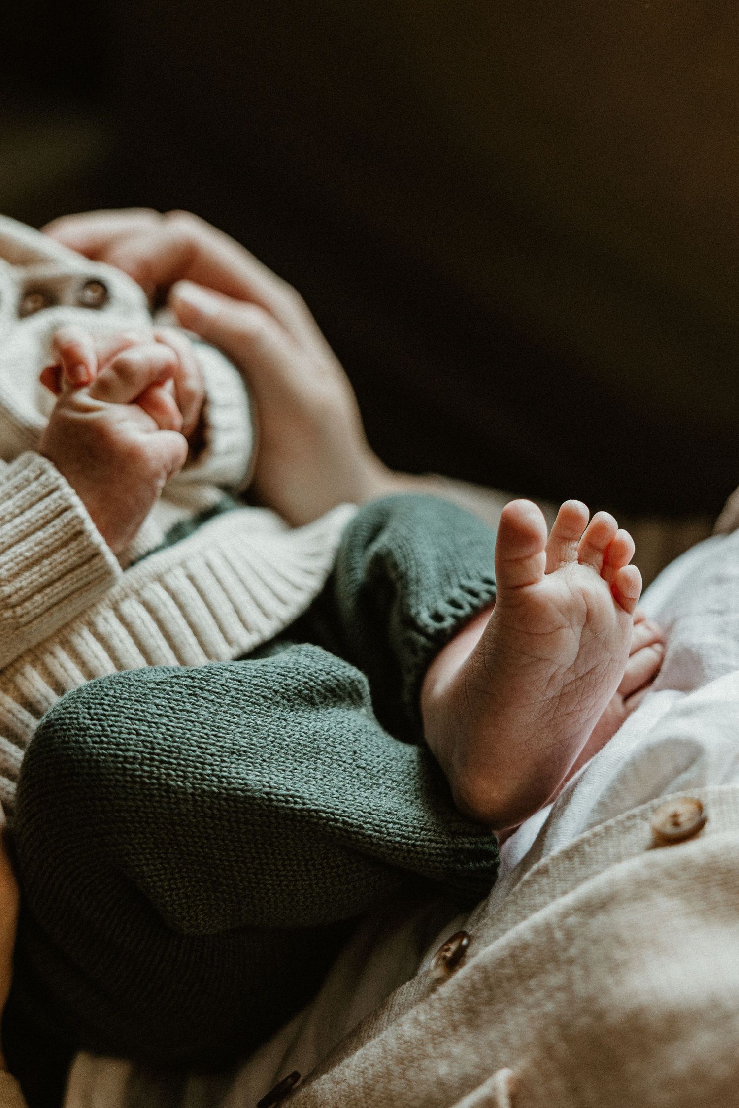 Close-up of tiny baby feet and legs in green pants against white fabric.