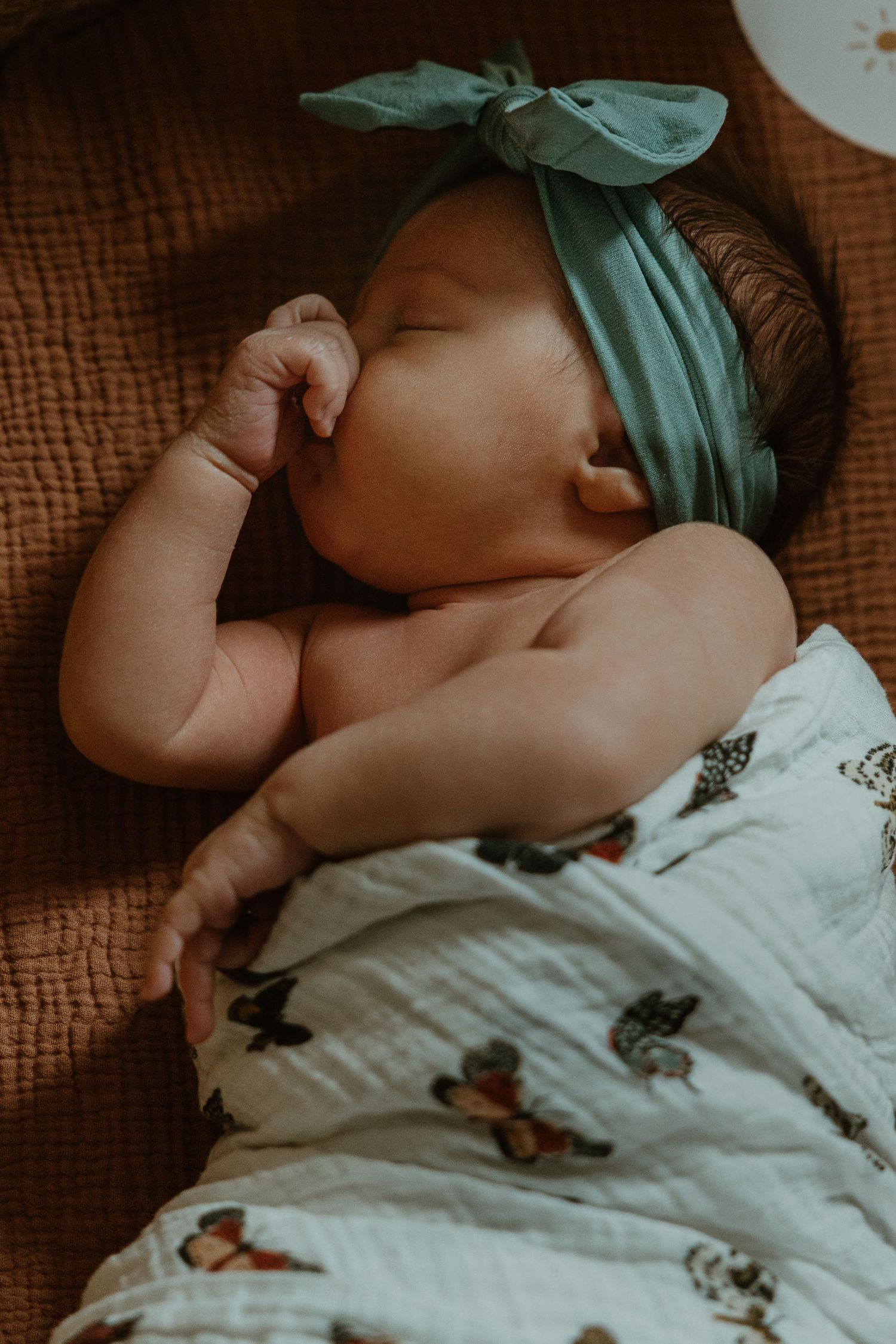 Sleeping newborn baby wearing a green bow headband wrapped in a white butterfly muslin swaddle blanket.