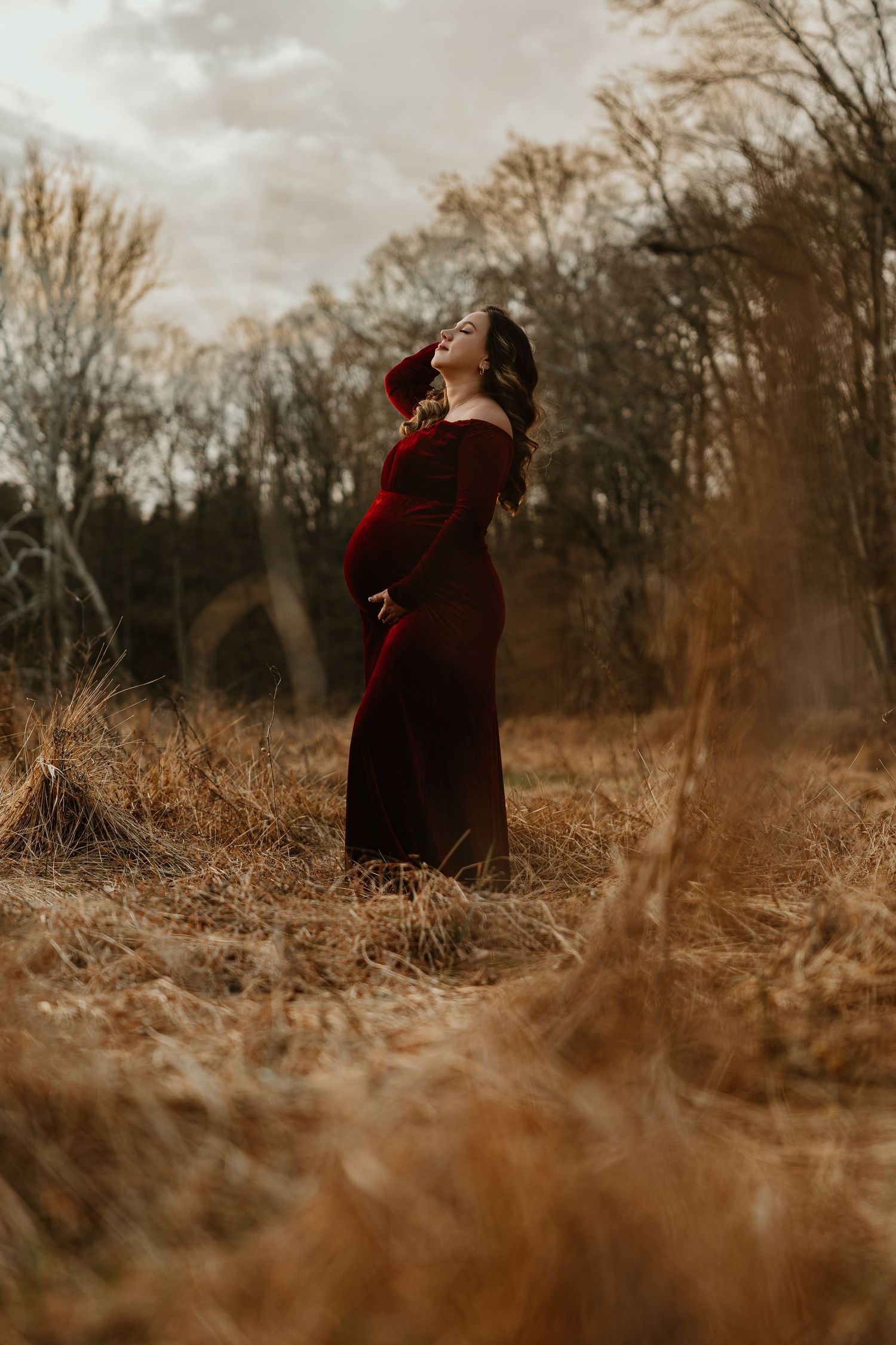Artistic low-angle shot through dried grass of someone in a burgundy dress in a fall setting.