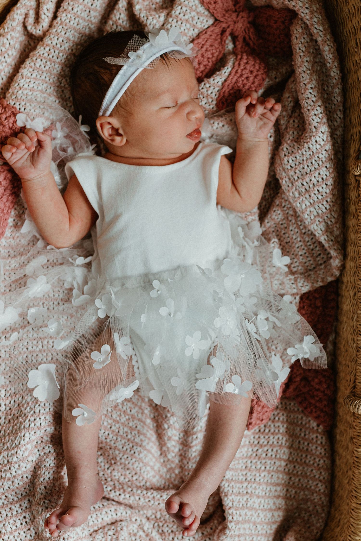 Newborn baby lying on textured blanket surrounded by delicate white feathers.