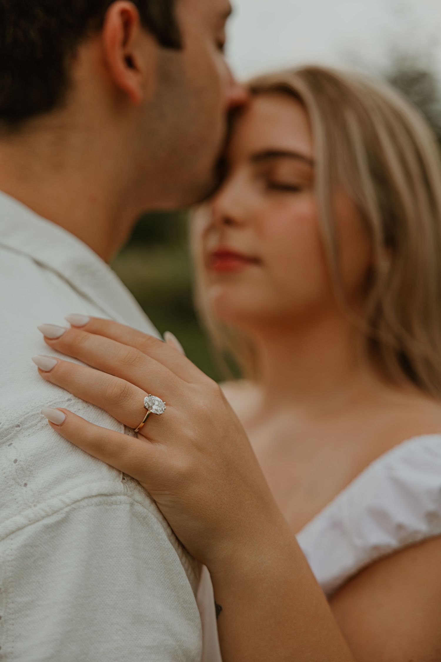 Couple sharing an intimate moment, woman displaying a sparkling diamond engagement ring on her hand against man's shoulder.