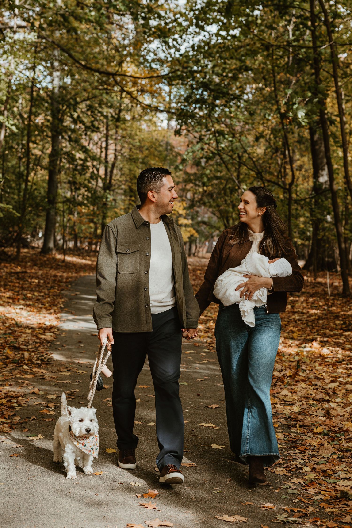 Couple walking with a white dog on a leaf-covered path in autumn.