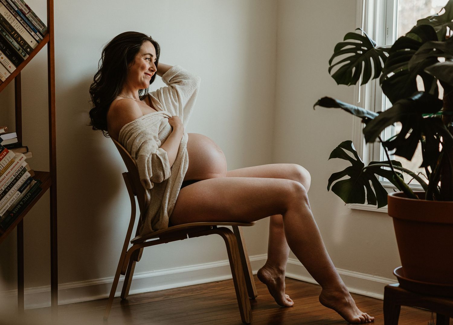 Candid maternity portrait with houseplant and natural window lighting.