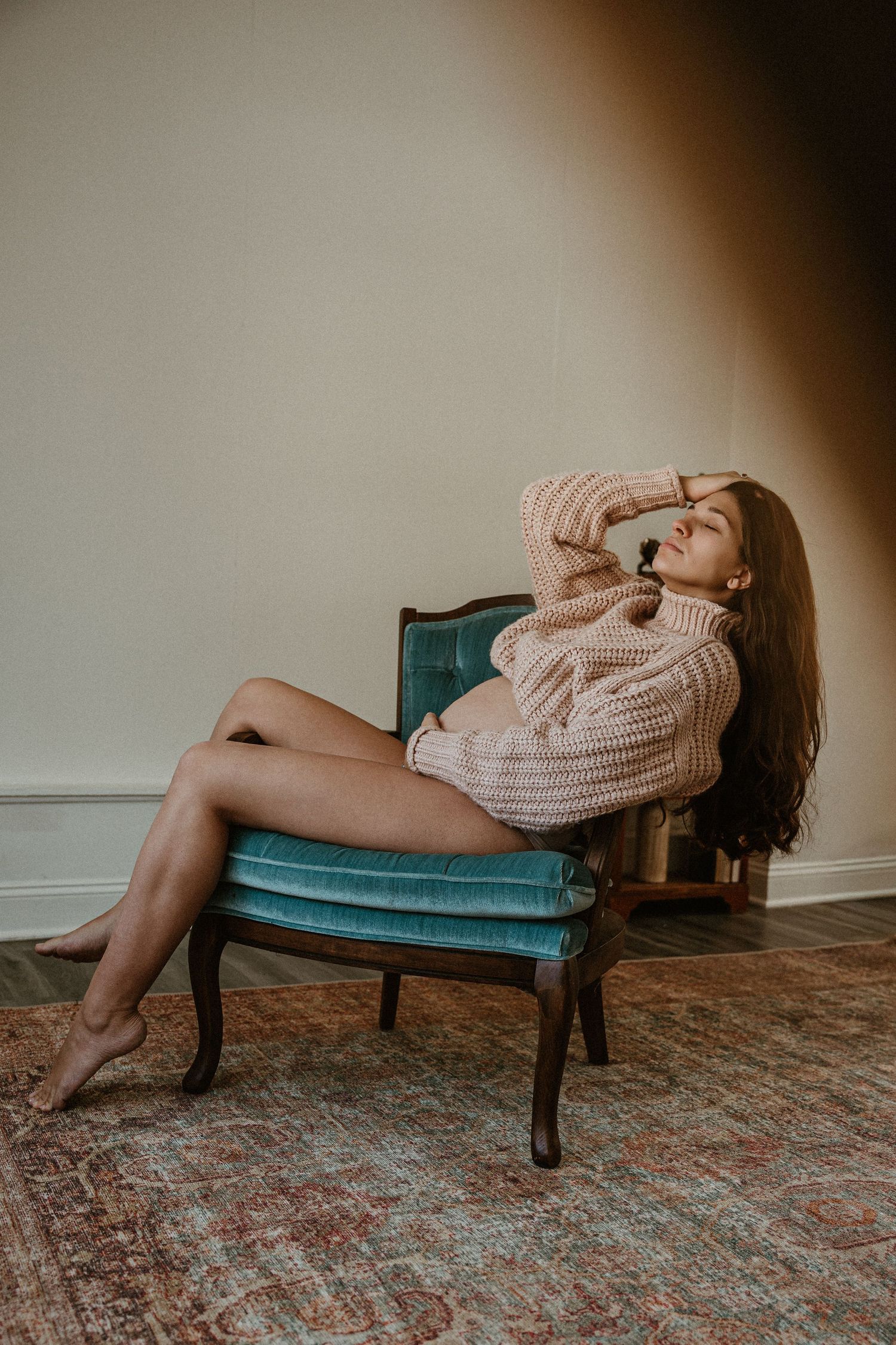 Cozy lifestyle portrait on teal velvet chair wearing oversized knit sweater.