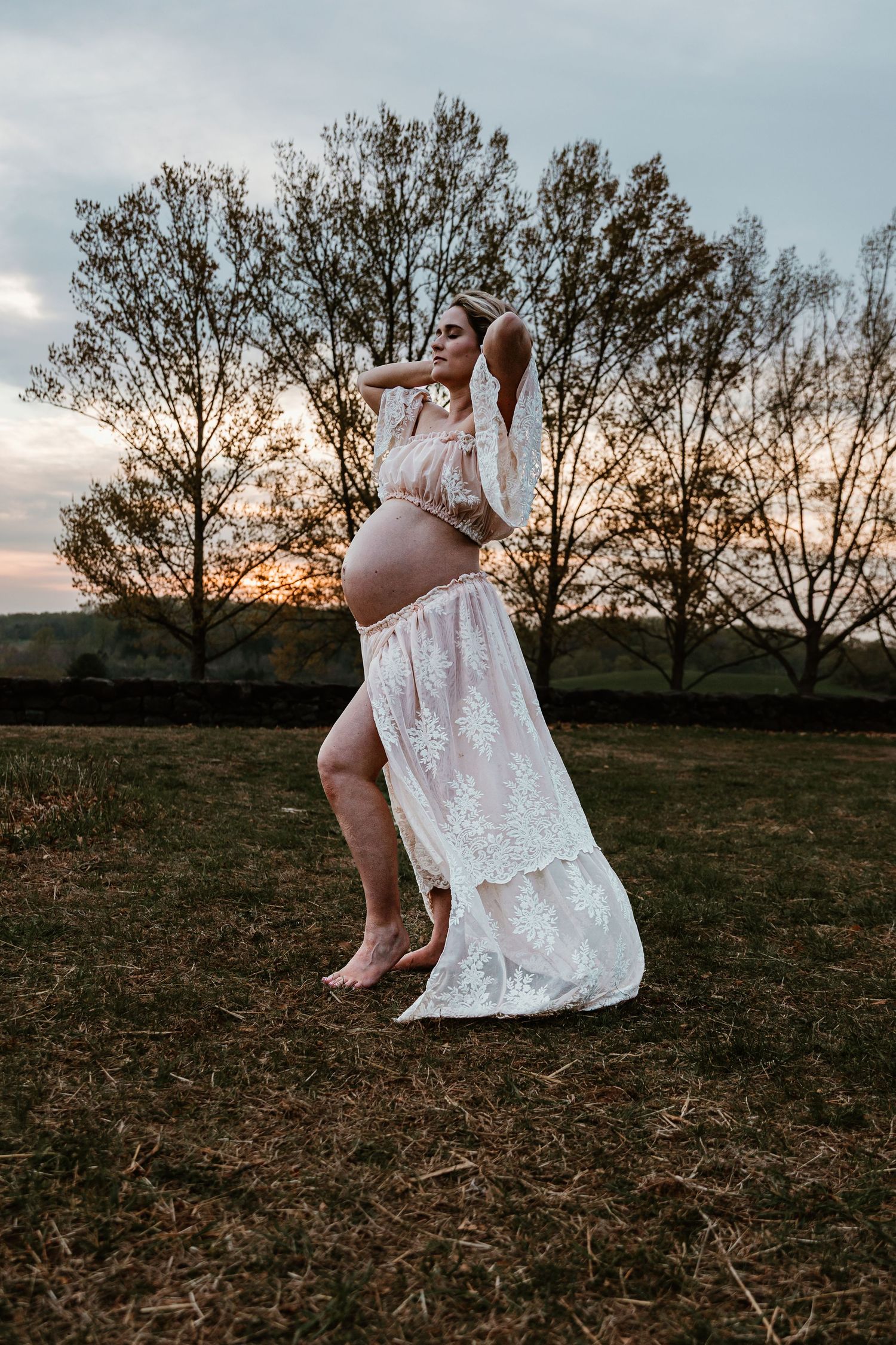 A flowing white lace dress catches evening light in a rustic outdoor setting.