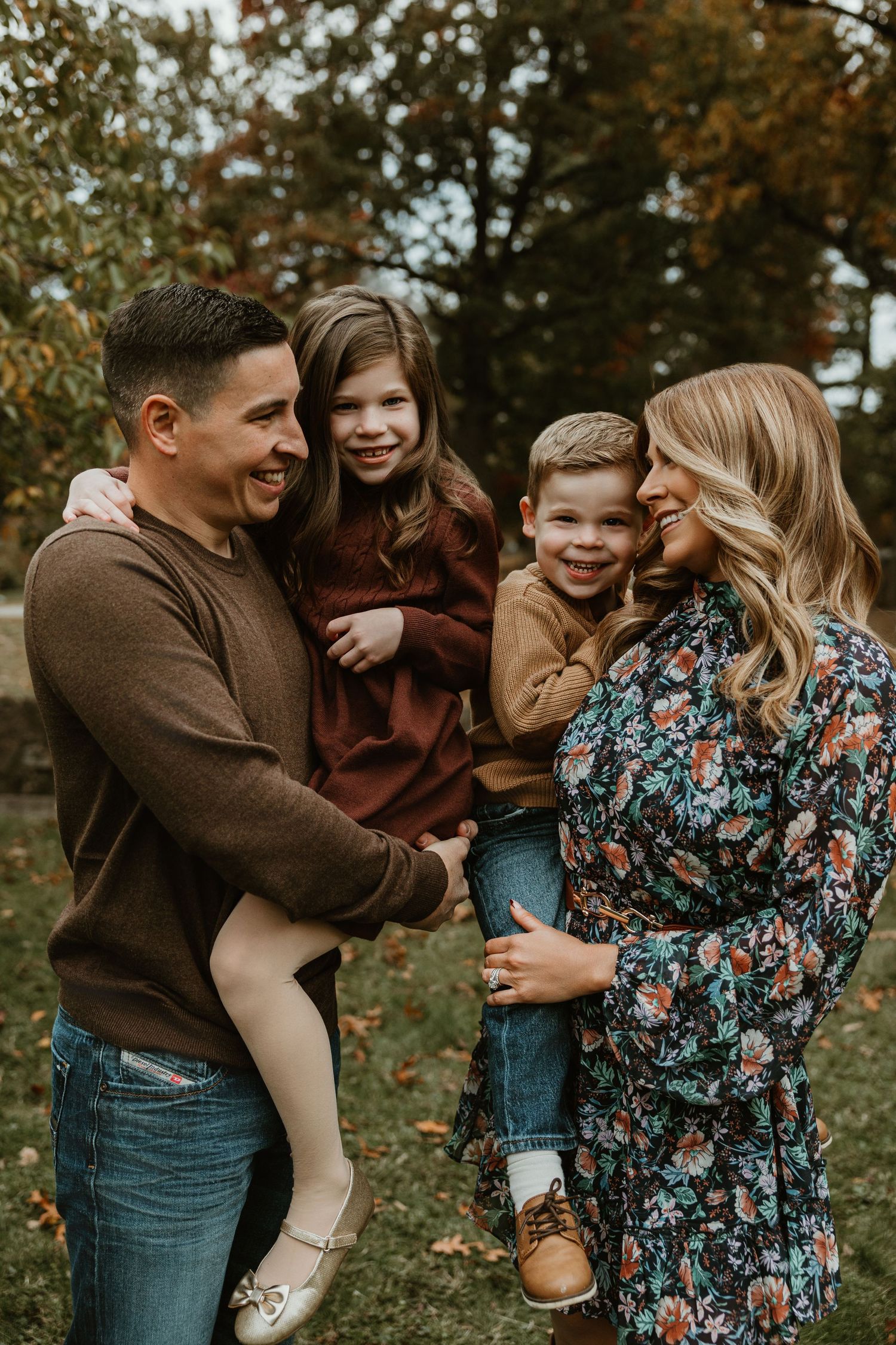 Family laughing and playing together during autumn outdoor photoshoot.