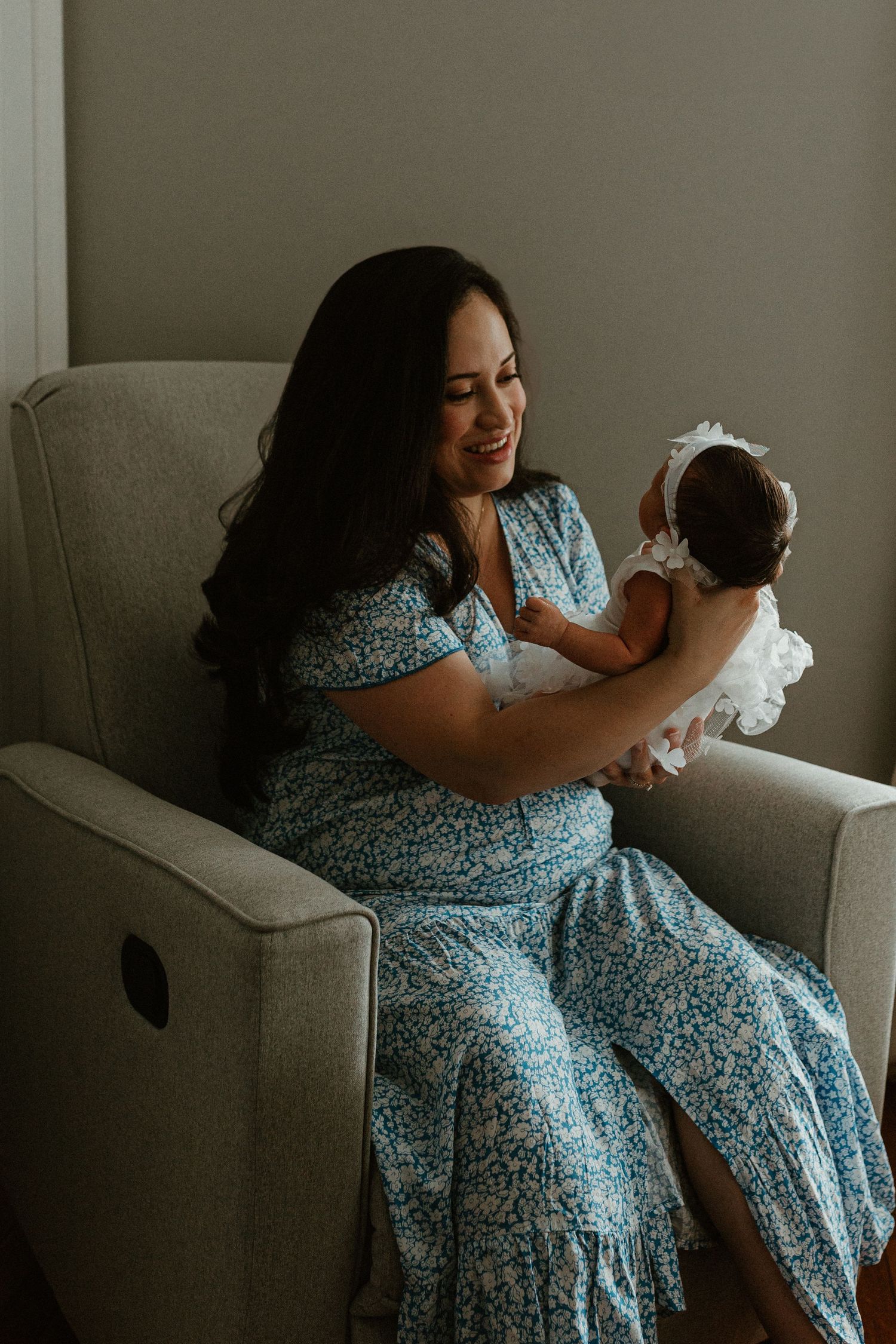 A woman in a blue floral dress sits comfortably on a gray armchair.